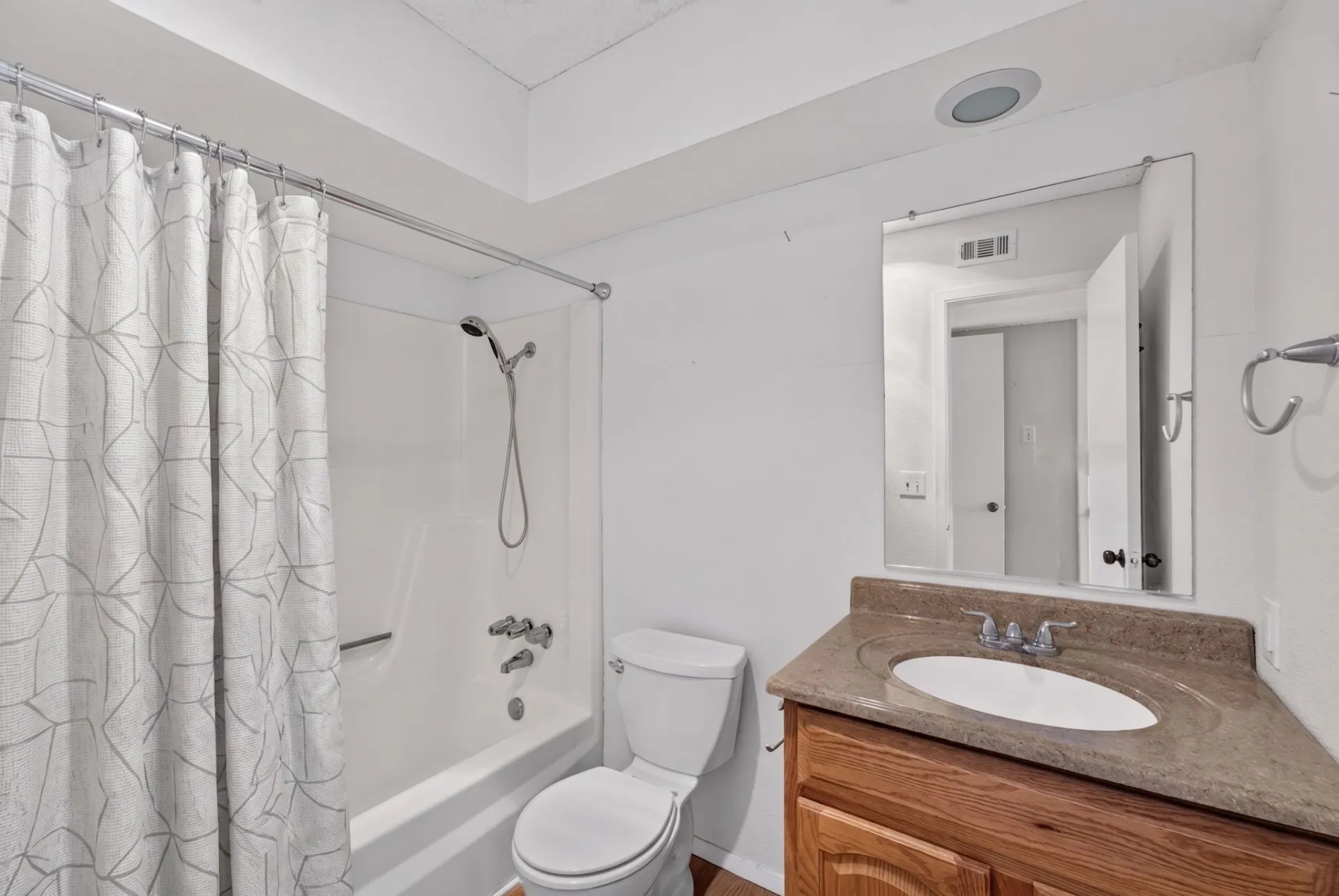 White bathtub with shower, wood-finish vanity with countertop, and toilet