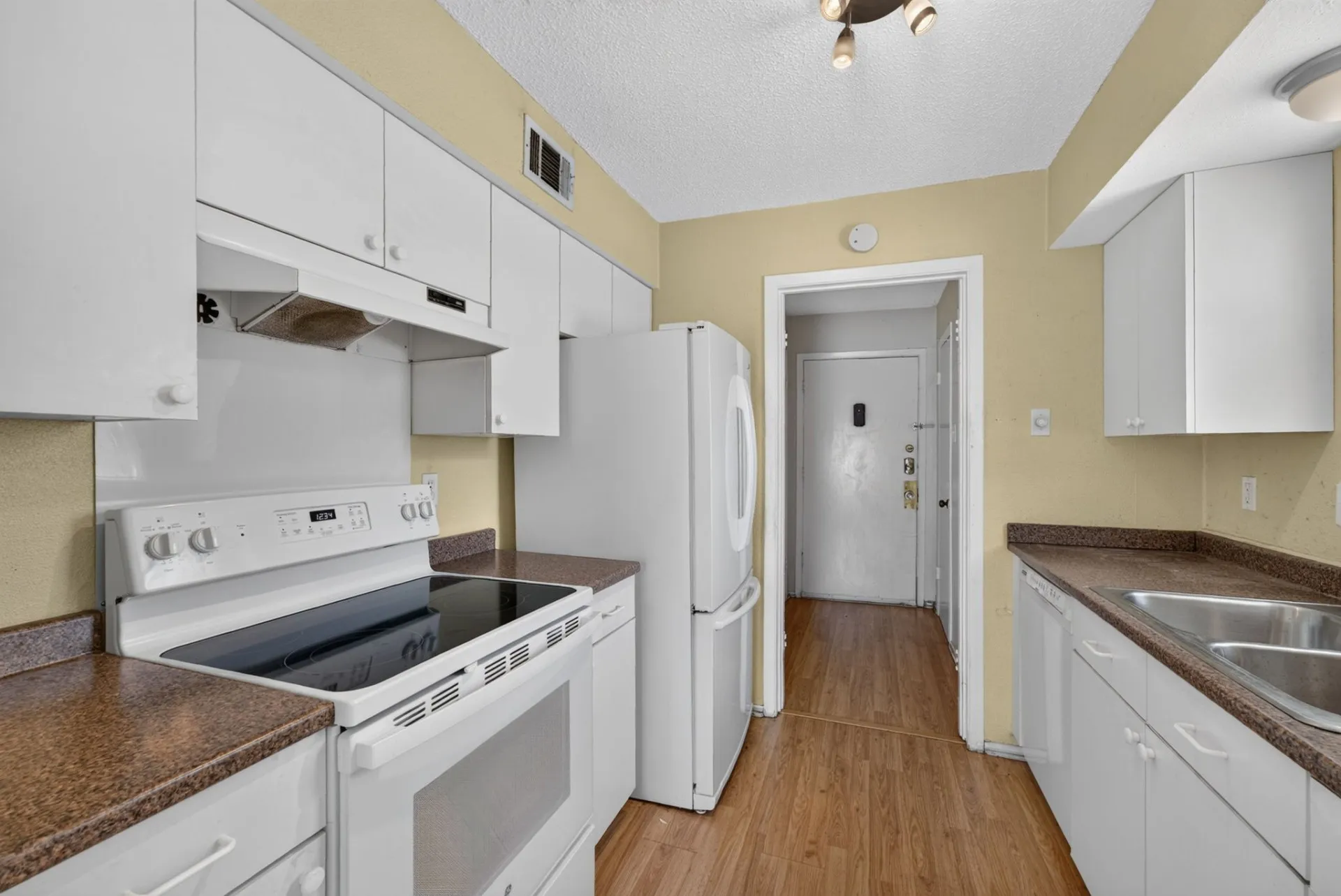 Galley kitchen featuring white cabinetry, brown-patterned countertops, wood-finish flooring, a white electric range, and a double basin stainless steel sink