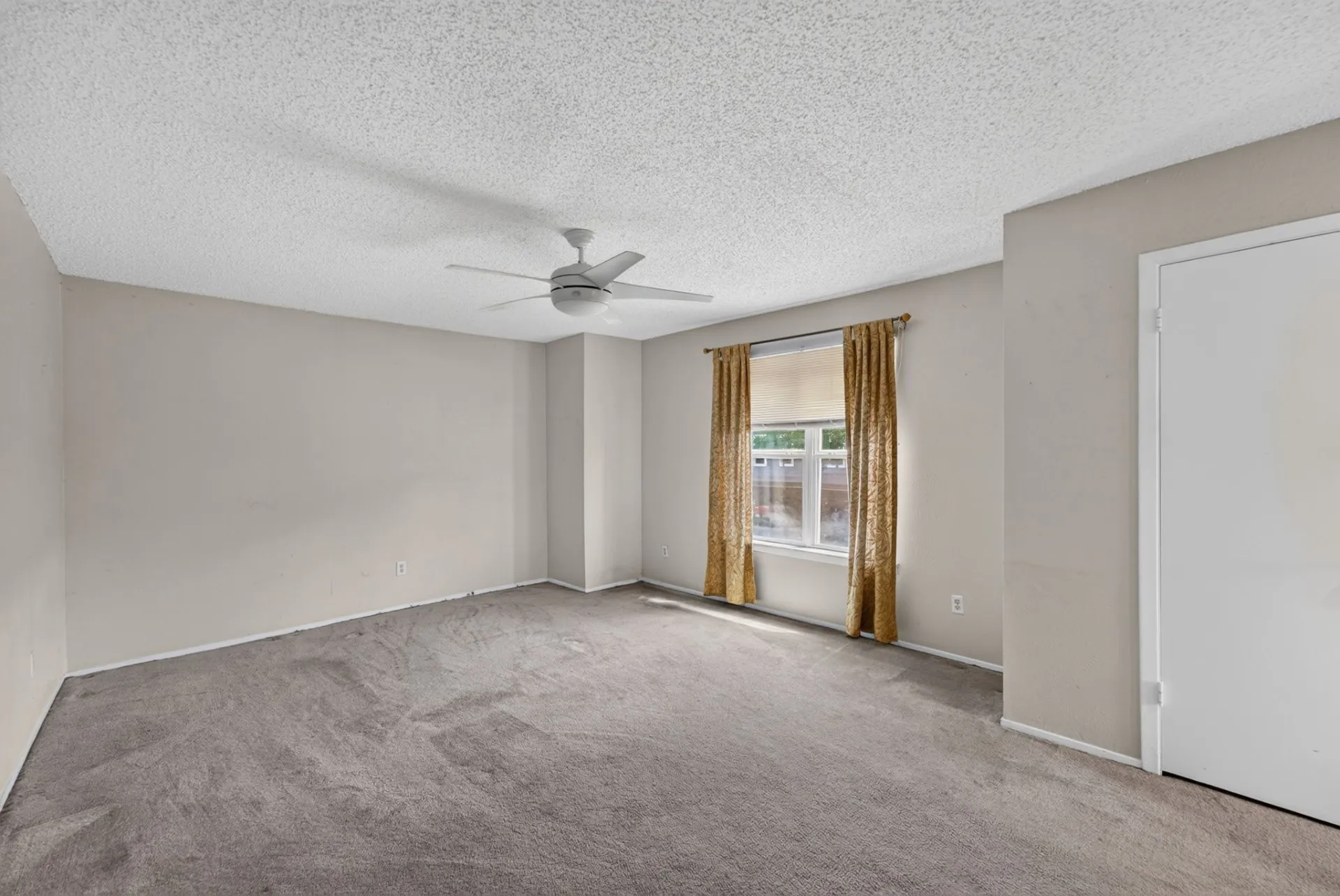 Spacious room featuring carpeting, a multi-pane window, and a ceiling fan