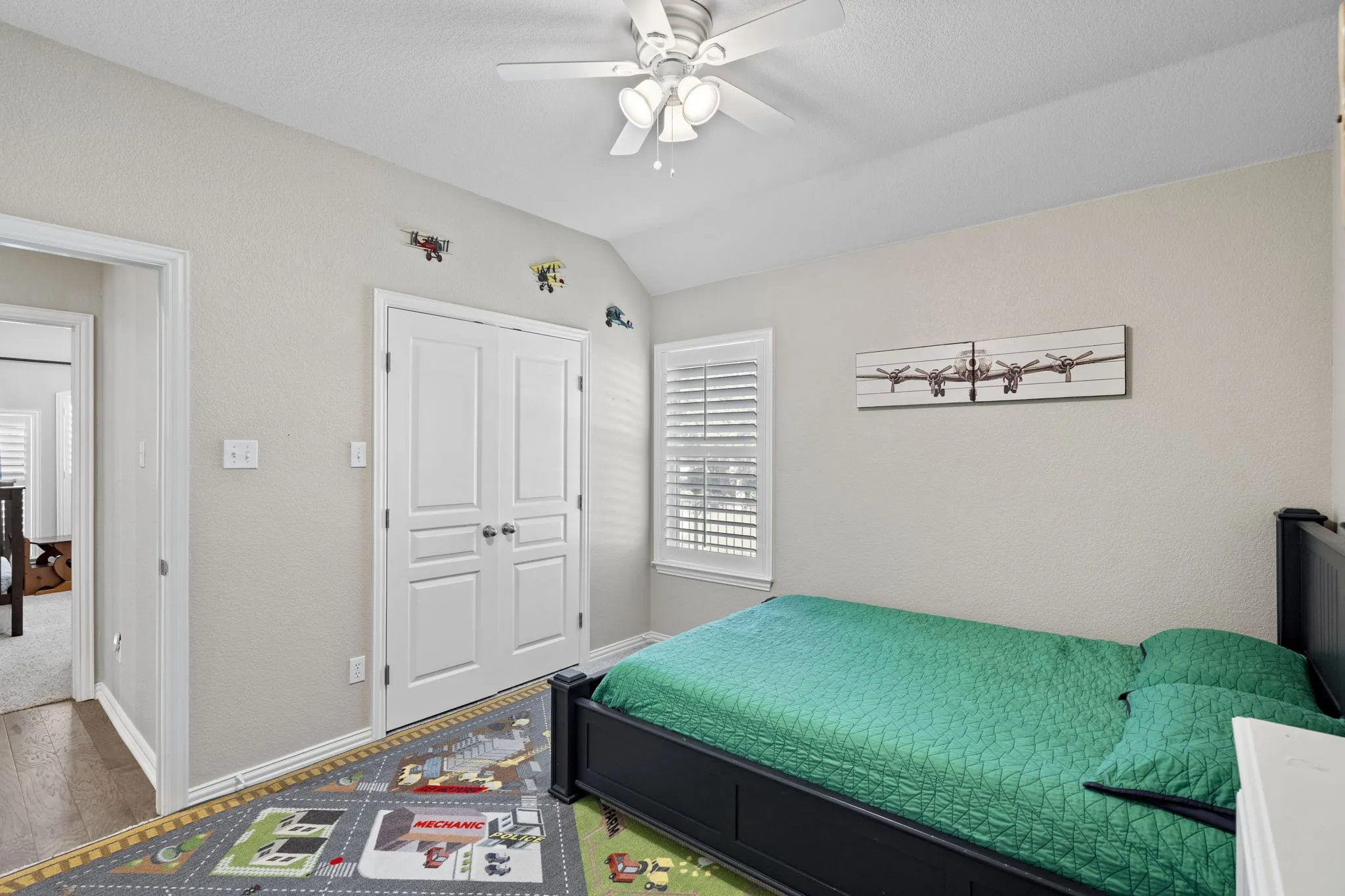 Vaulted ceiling with a ceiling fan, window with plantation shutters, double closet doors, and wood-finish flooring