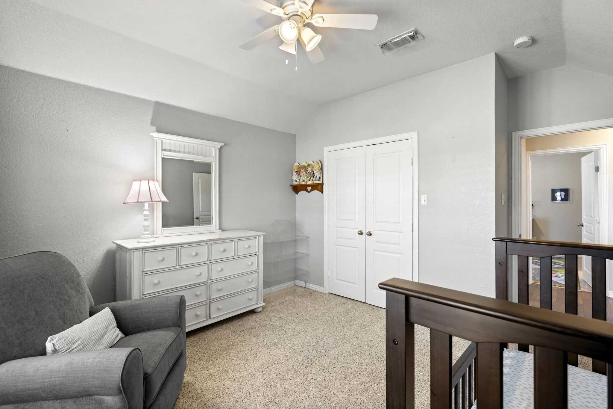 Vaulted ceiling, ceiling fan, neutral carpet, wood-finish railing, and white double-door closet