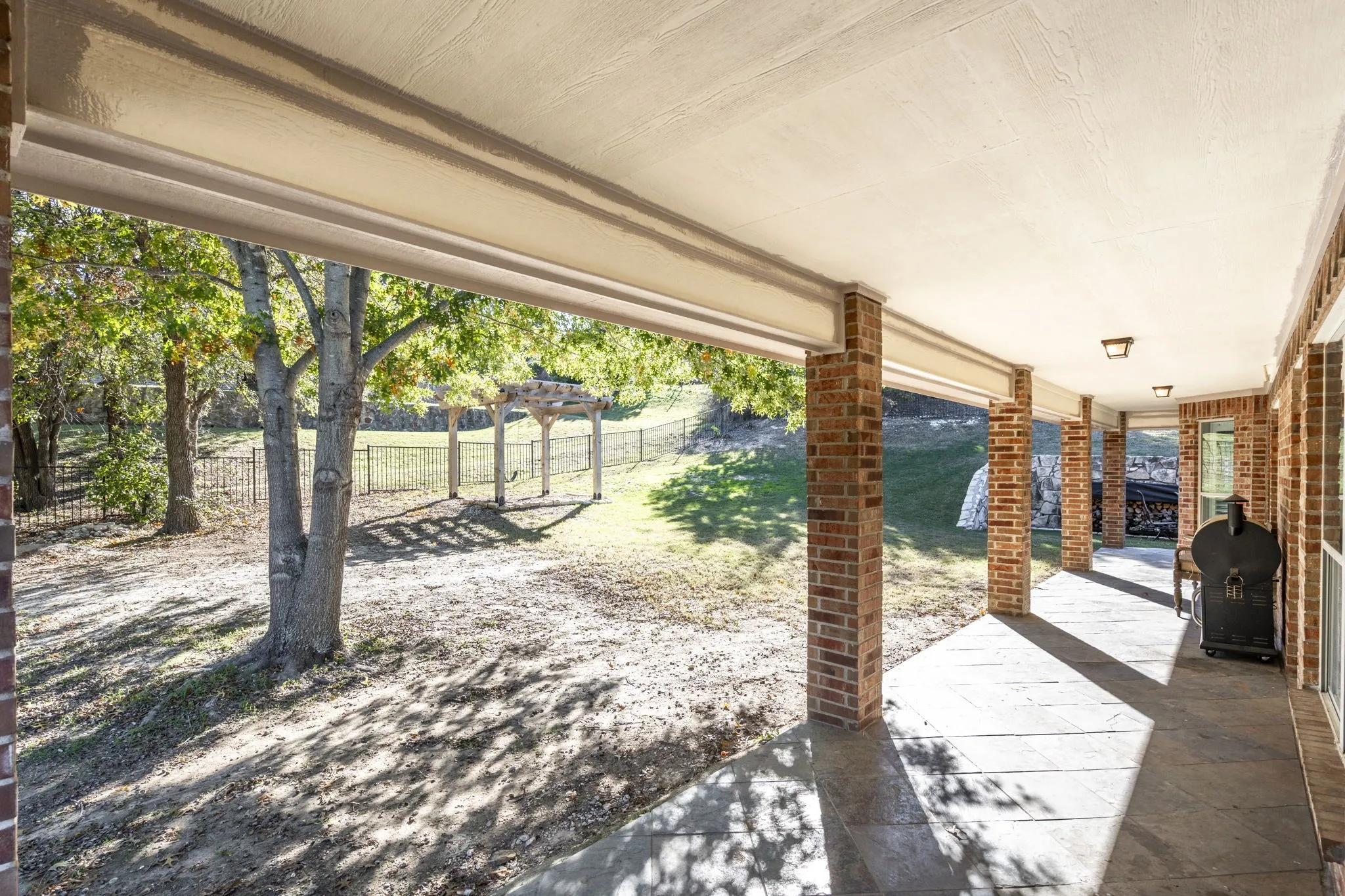 Brick columned covered patio with concrete flooring, recessed lighting, and a fenced backyard