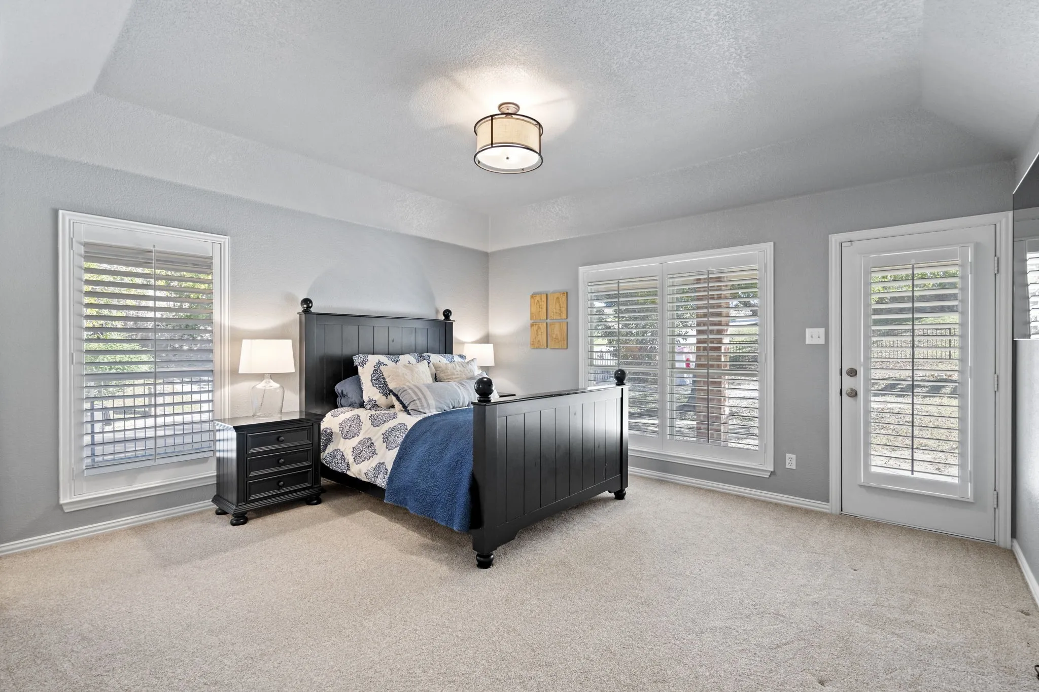 Vaulted ceiling, two large windows with plantation shutters, a glass-paneled exterior door with plantation shutters, and light-toned carpet flooring
