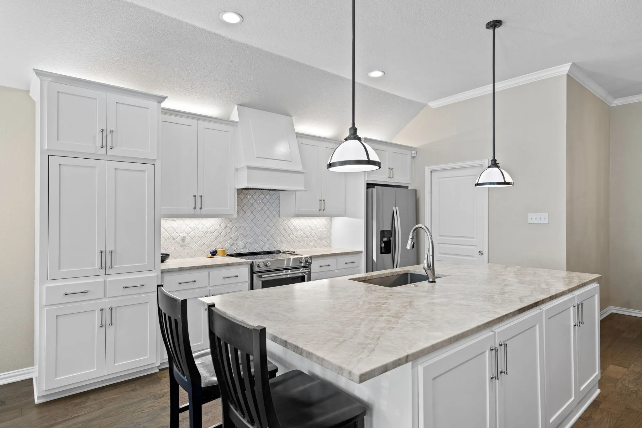 Bright kitchen featuring white shaker-style cabinetry, a large kitchen island with integrated sink, stainless steel appliances, and recessed lighting