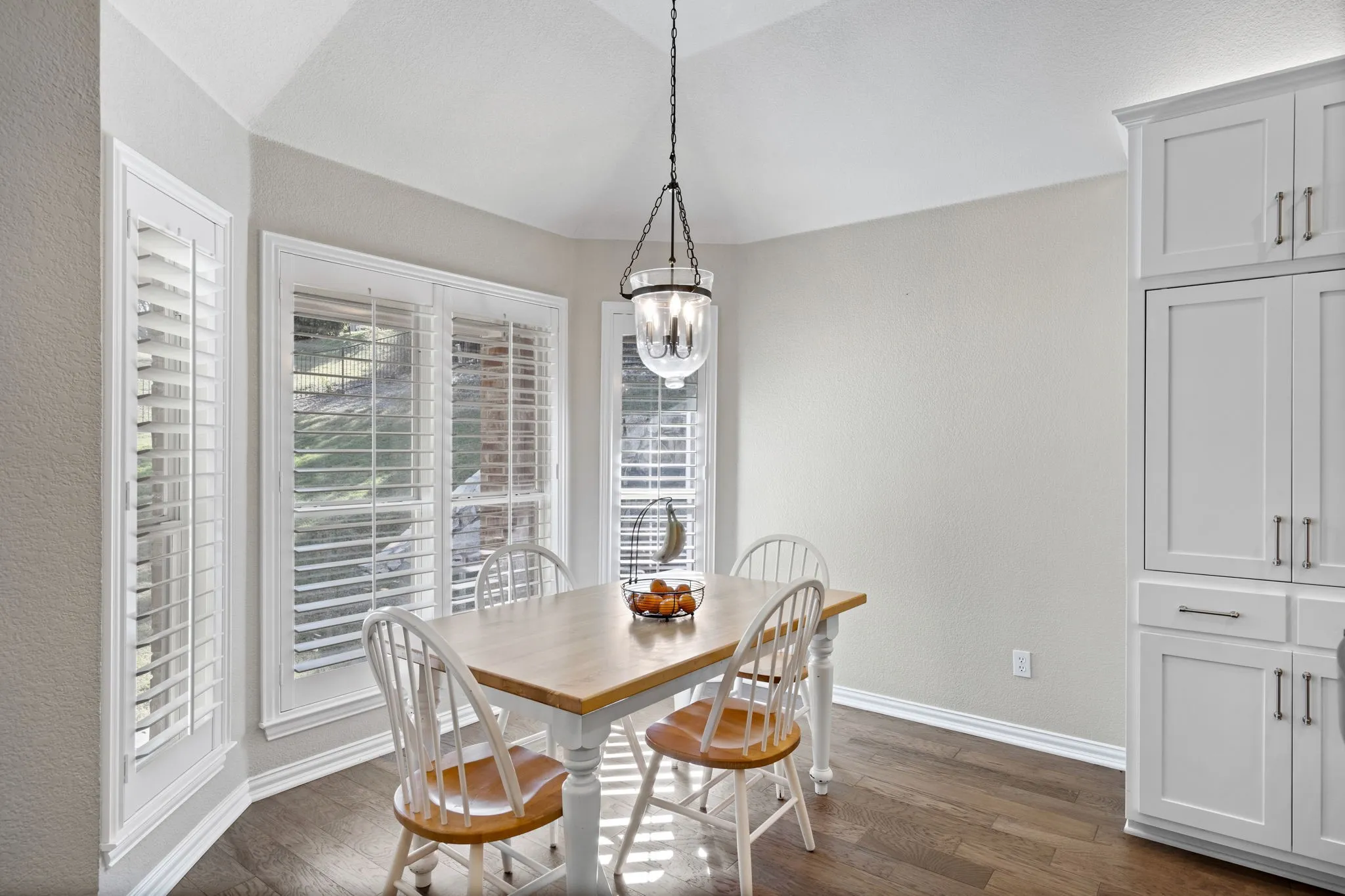Vaulted ceiling with a chandelier, wood-finish flooring, white plantation shutters, and built-in white cabinetry with silver hardware