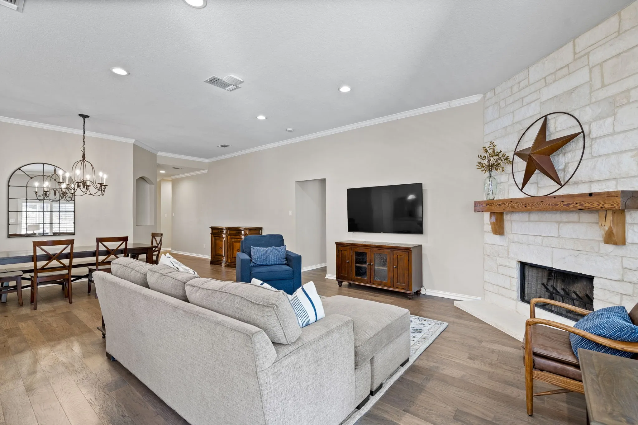 Stone-clad fireplace with a natural wood mantel, wood-finish flooring, recessed lighting, and a chandelier in the dining area