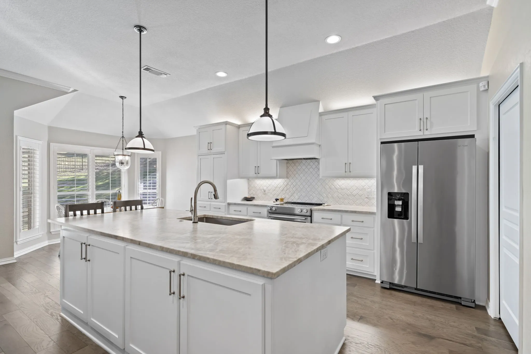 Kitchen featuring a large island with sink, white shaker cabinetry, stainless steel appliances, and wood-finish flooring