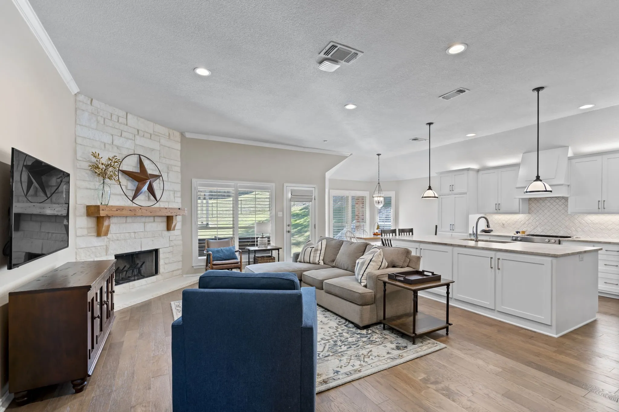 Open-concept living space featuring a stone-clad fireplace with a wood mantel, wood-finish flooring, and recessed lighting
