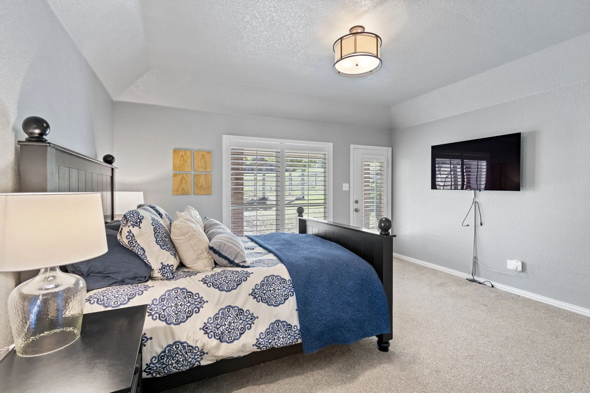 Vaulted ceiling, ceiling-mounted light fixture, carpeted flooring, sliding glass door, and a single-panel door with louvered shutters