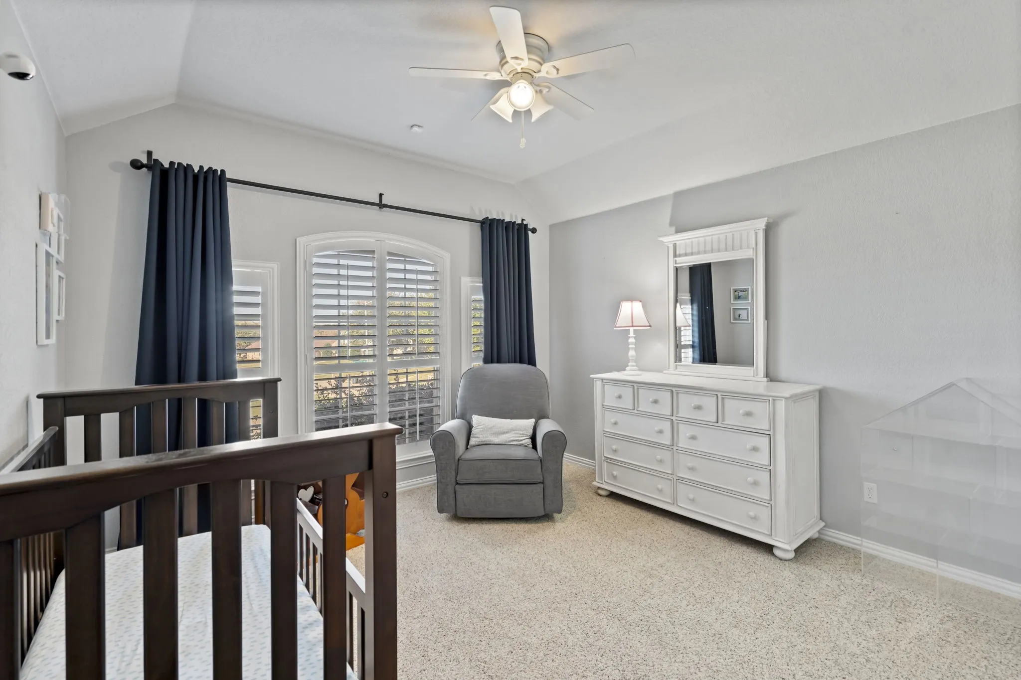 Vaulted ceiling with a ceiling fan, arched window with plantation shutters, wall-to-wall carpeting, and crown molding