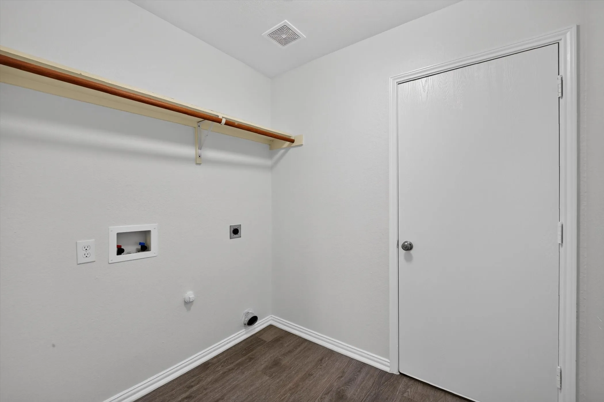 Utility space featuring wood-finish flooring, white walls, and a built-in shelf with hanging rod