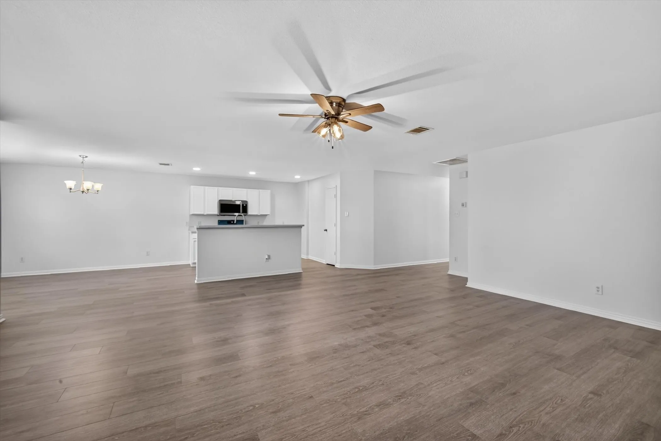 Wood-finish flooring, recessed lighting, ceiling fan, white wall paint, and white cabinetry