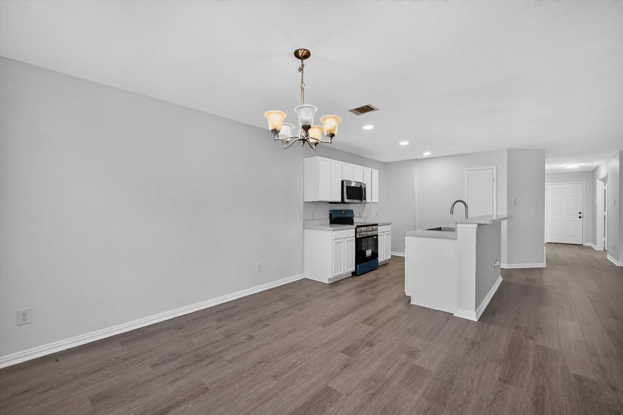 Open-concept living area featuring wood-finish flooring, a contemporary chandelier, white cabinetry, integrated microwave, and a kitchen island with a single-basin sink