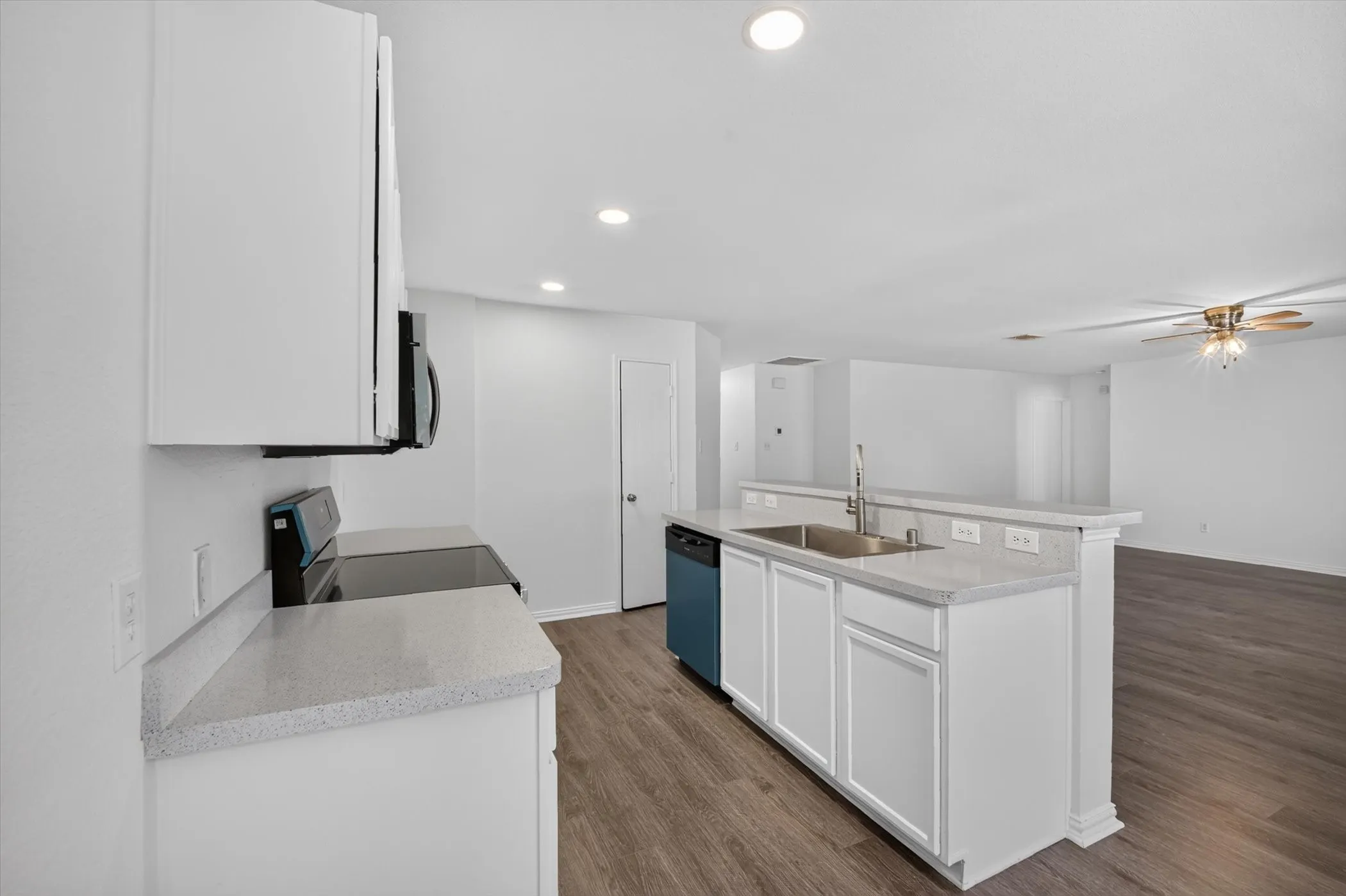 Spacious kitchen featuring an island with a stainless steel sink, white cabinetry, integrated appliances, and wood-finish flooring