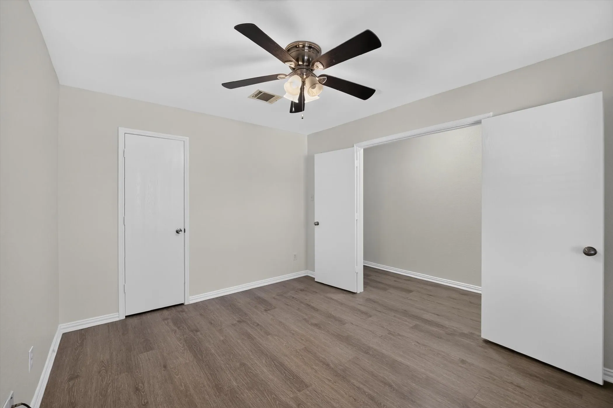 Wood-finish flooring, light neutral wall paint, and a ceiling fan with integrated lighting