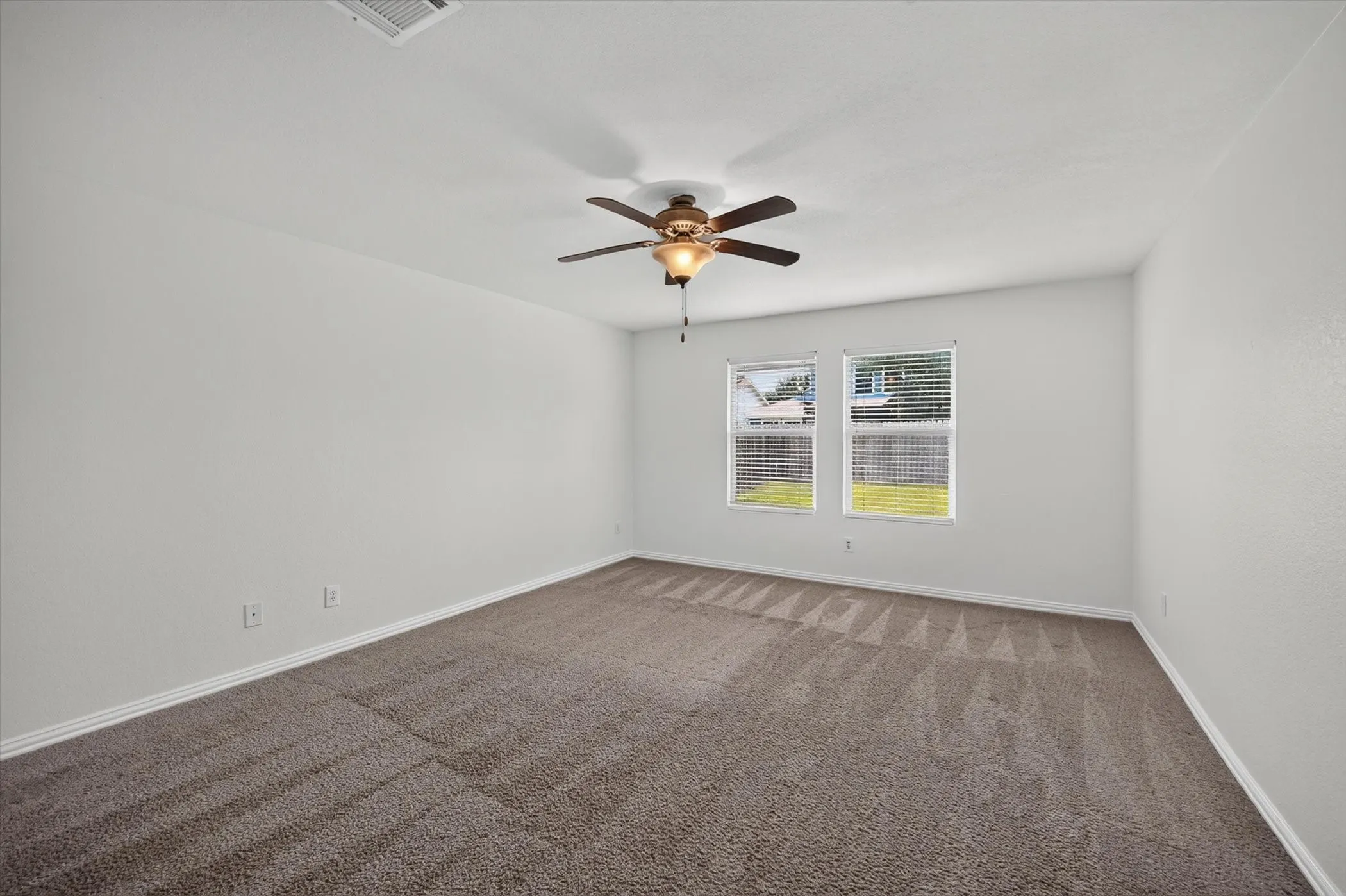 Spacious room with plush carpeting, two large windows, and a ceiling fan with integrated lighting