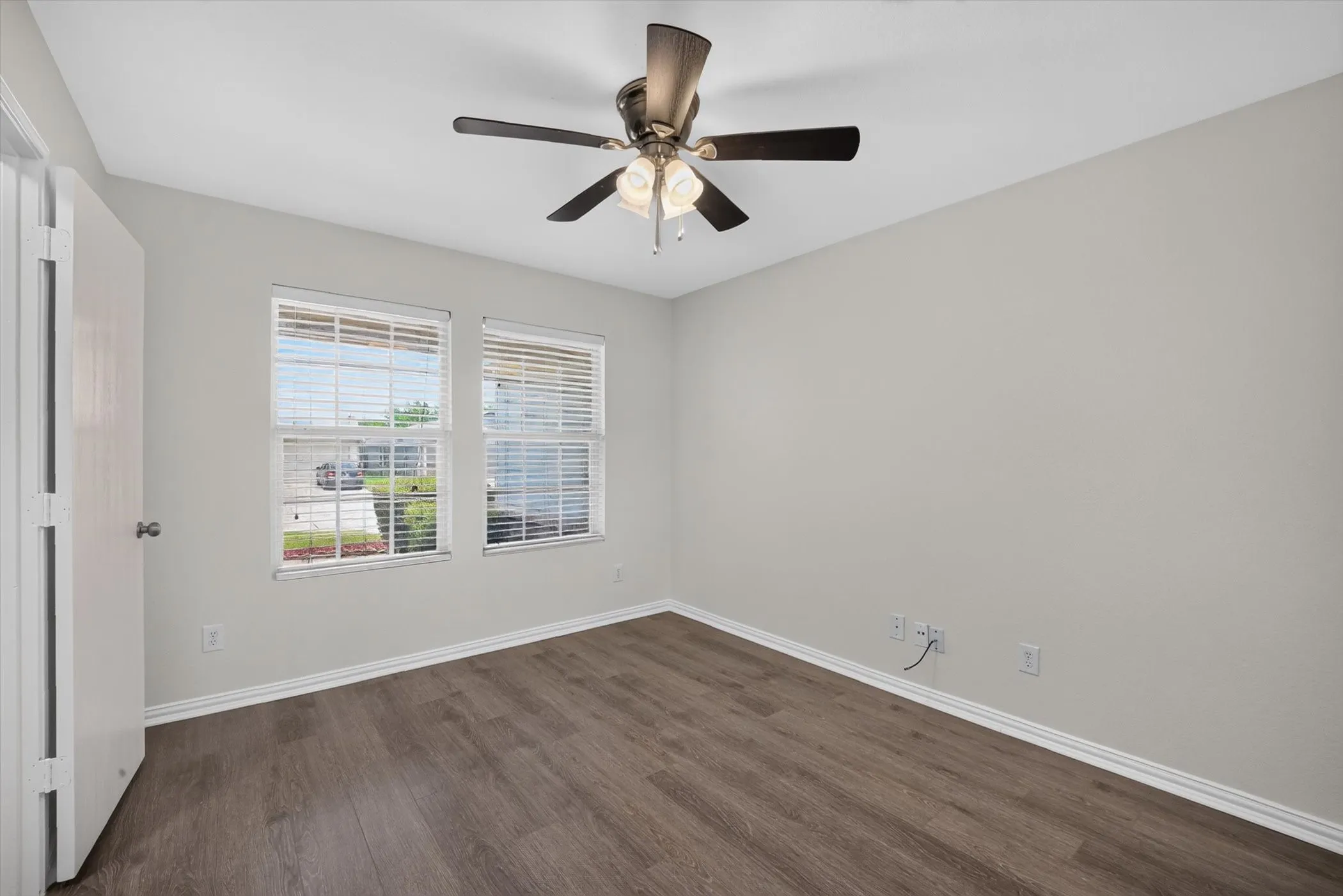 Wood-finish flooring, ceiling fan with integrated lighting, two windows with blinds, and white trim