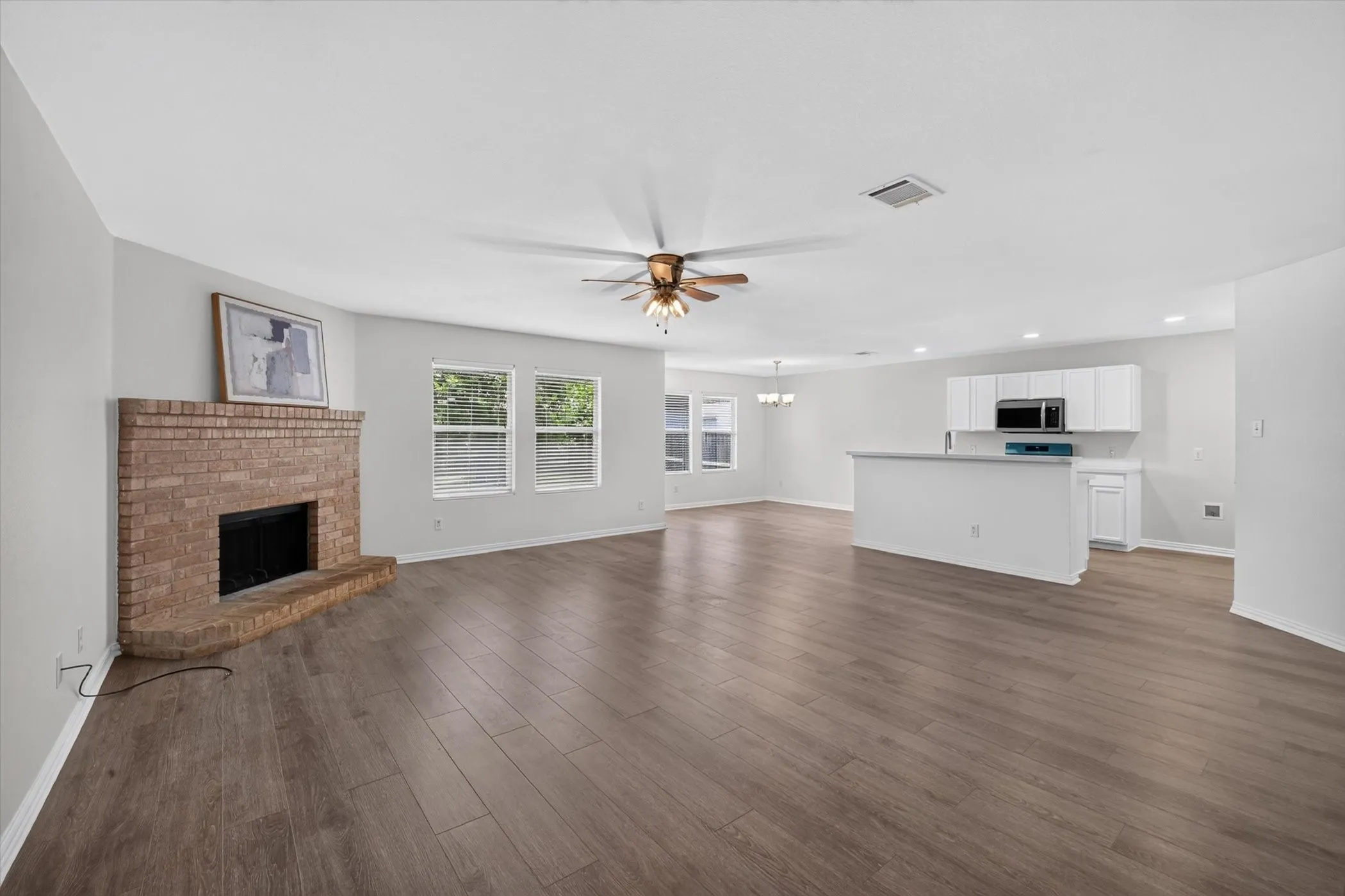 Open concept living space featuring wood-finish flooring, a brick fireplace, and multiple windows