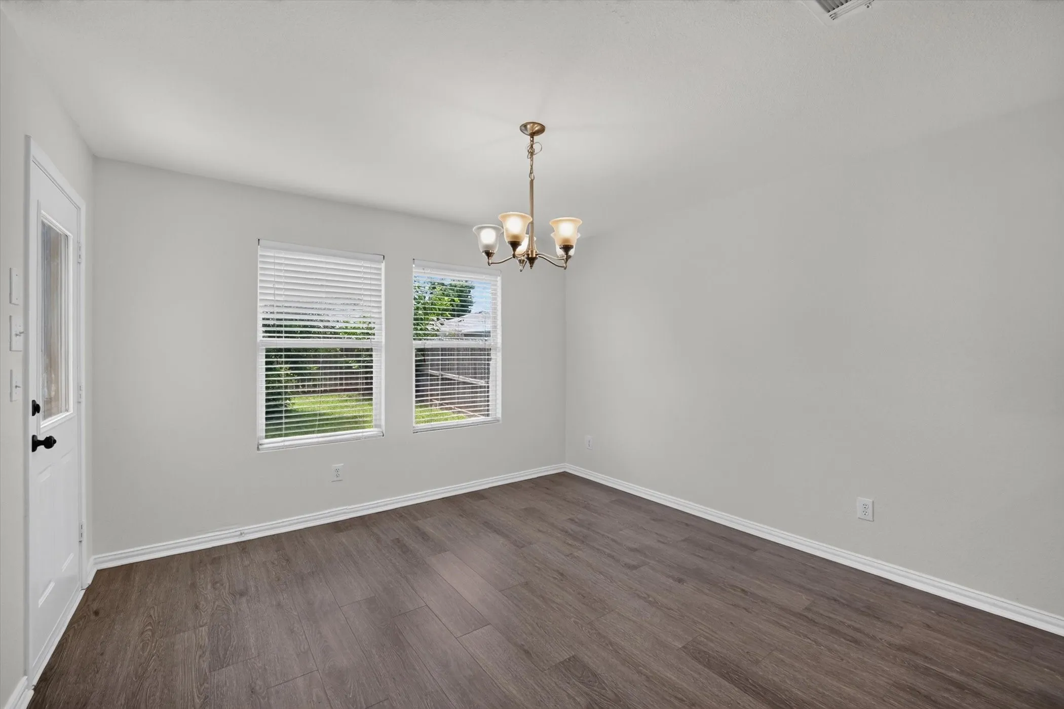 Wood-finish flooring, two windows with blinds, a ceiling-mounted light fixture, and a door with a glass insert
