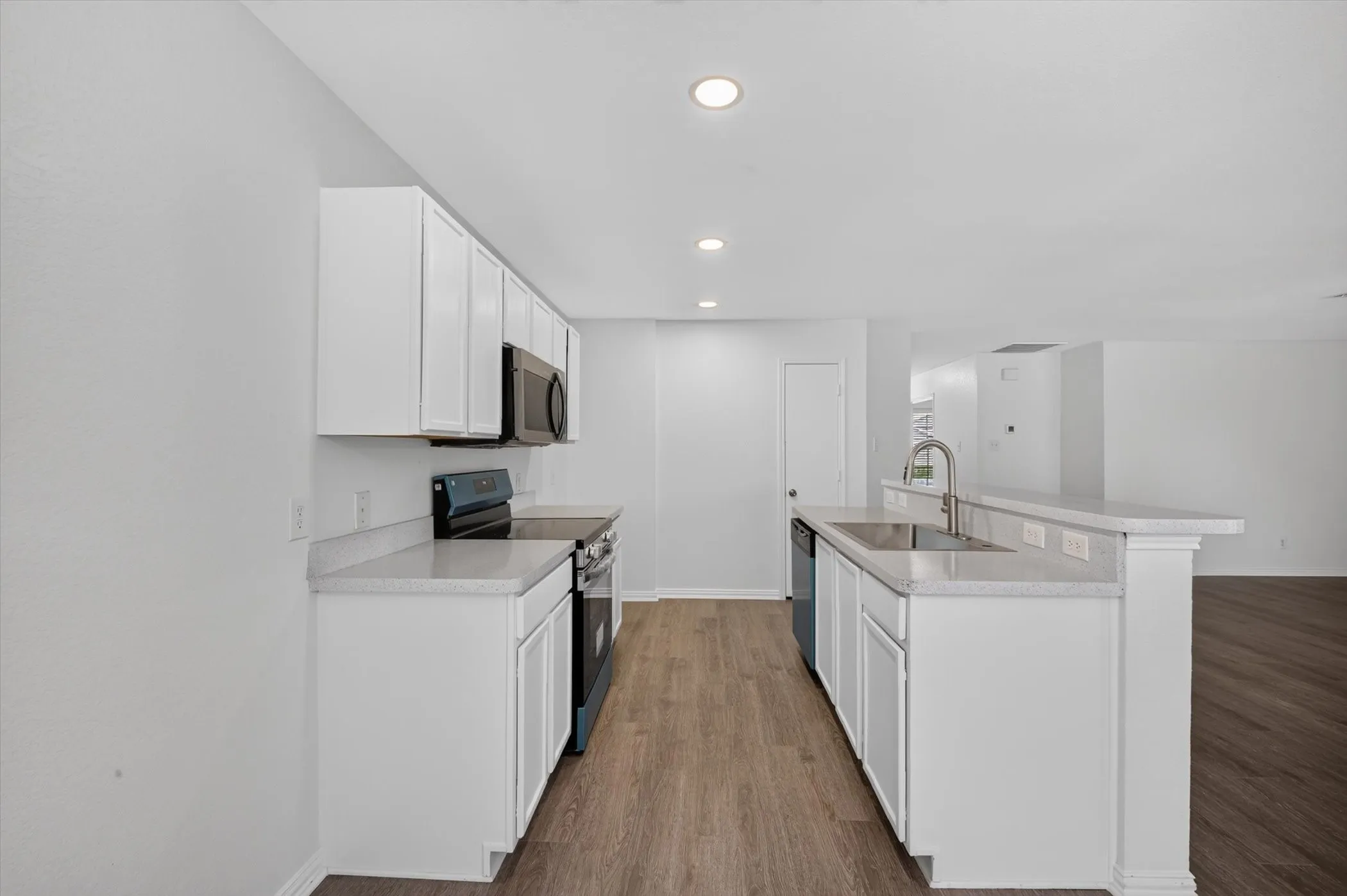 Kitchen featuring white cabinetry, light countertops, stainless steel sink, black appliances, and wood-finish flooring
