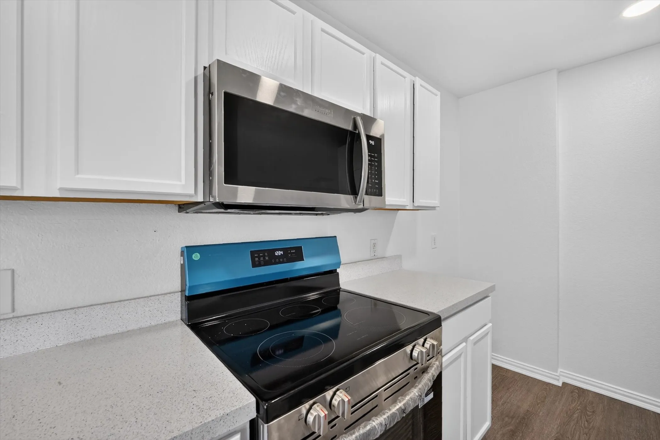 Kitchen featuring white cabinetry, stainless steel microwave, electric range, and light-toned countertops