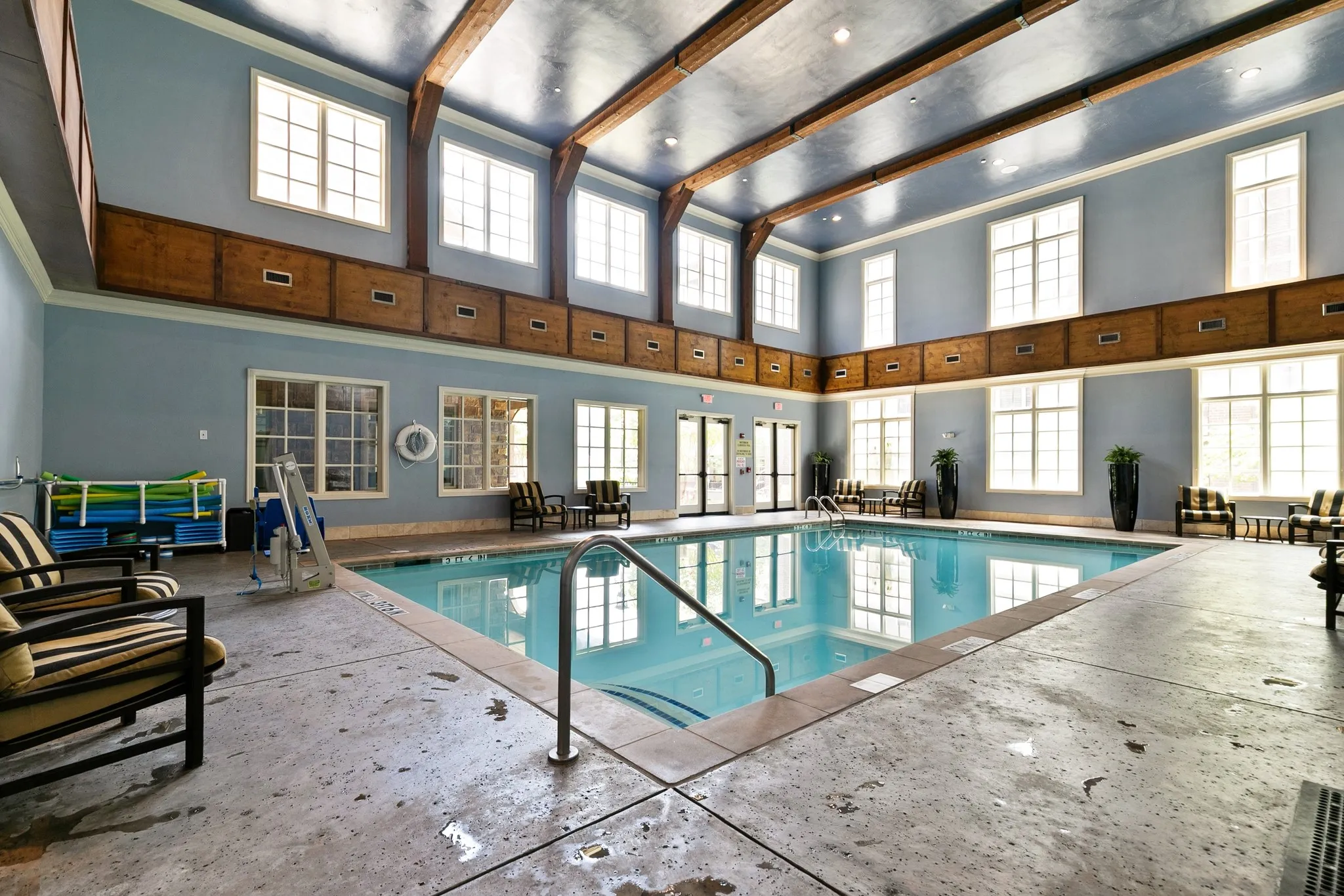 Indoor swimming pool with concrete decking, exposed wood beam ceiling, multiple transom windows, and double glass-paneled doors