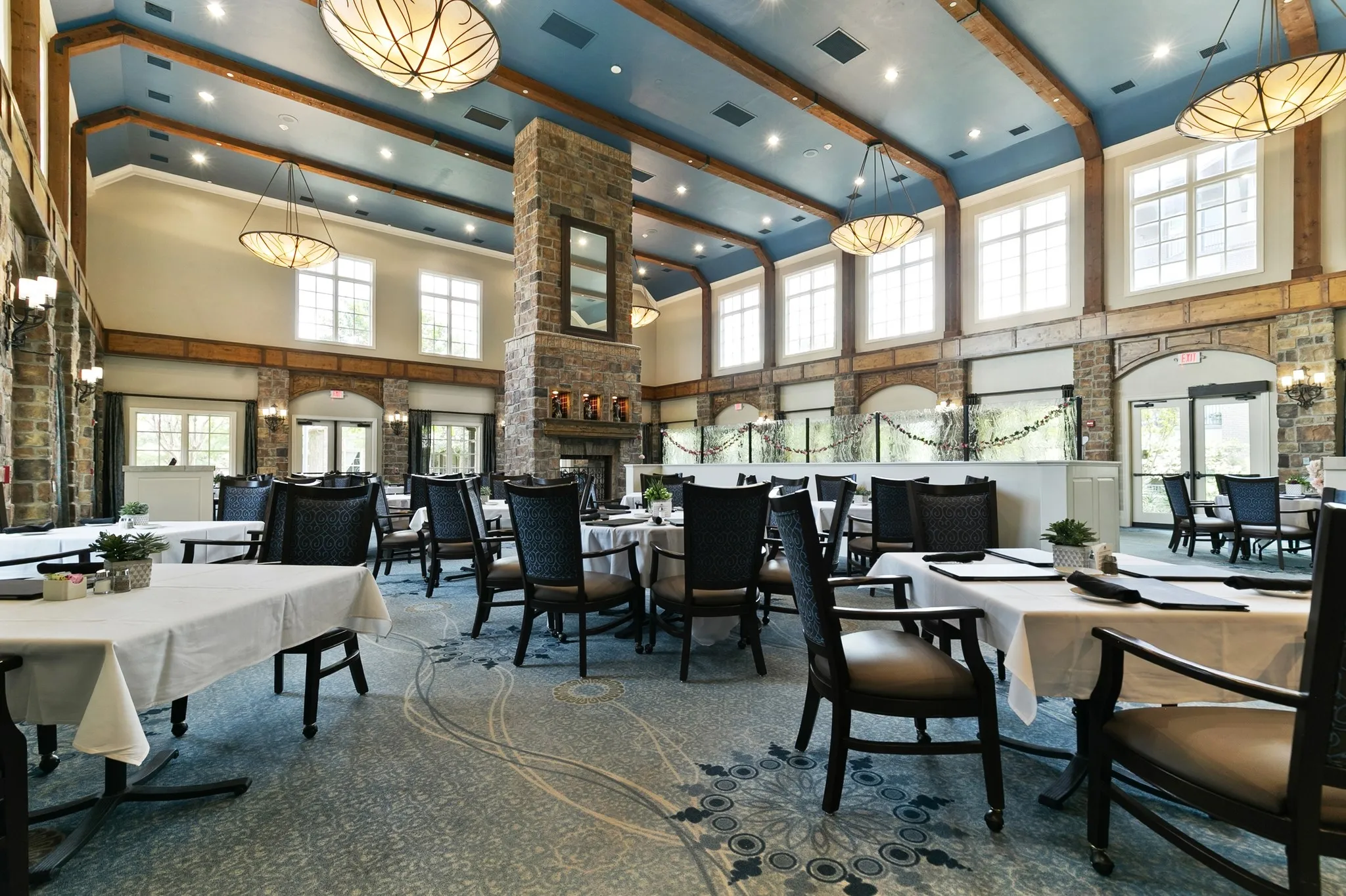 Spacious dining area featuring a stone fireplace, exposed wood beams, and a patterned carpet