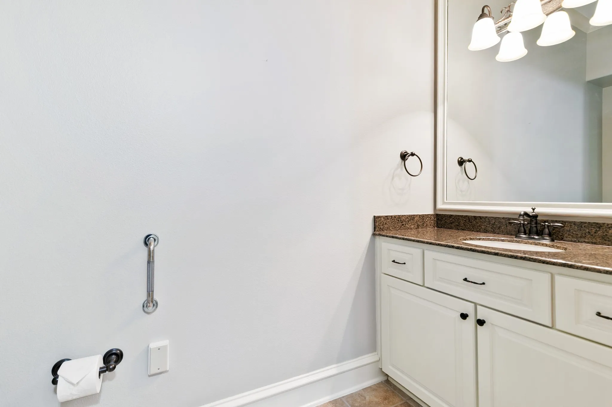 Half Bath. White vanity cabinetry with dark hardware, stone-finish countertop, undermount sink, and wall-mounted mirror with integrated lighting