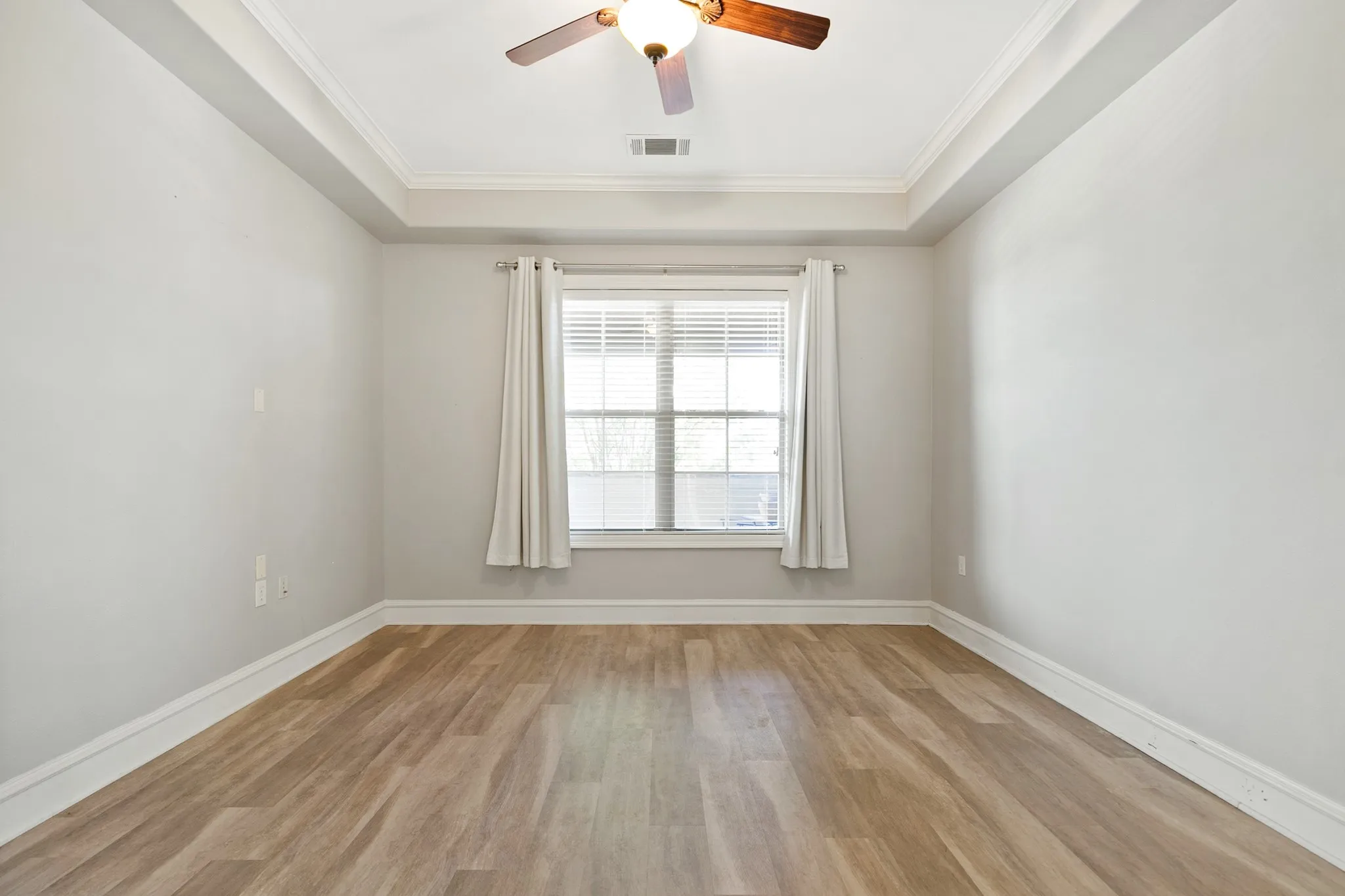 Recessed ceiling with crown molding, ceiling fan with light fixture, and a window with blinds