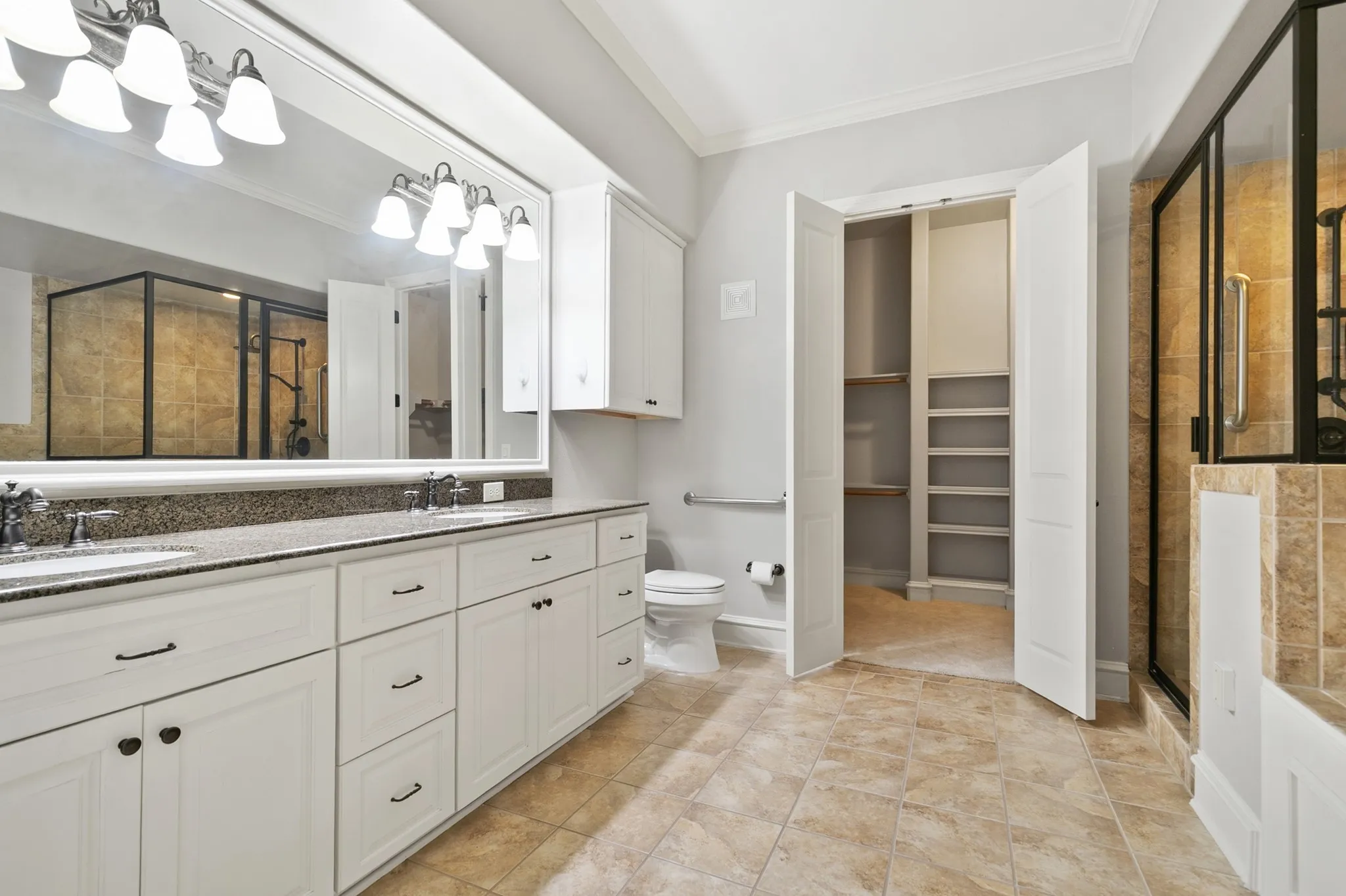 Dual vanity with integrated sinks, expansive mirror, glass-enclosed shower with tiled surround, and a walk-in closet with built-in shelving