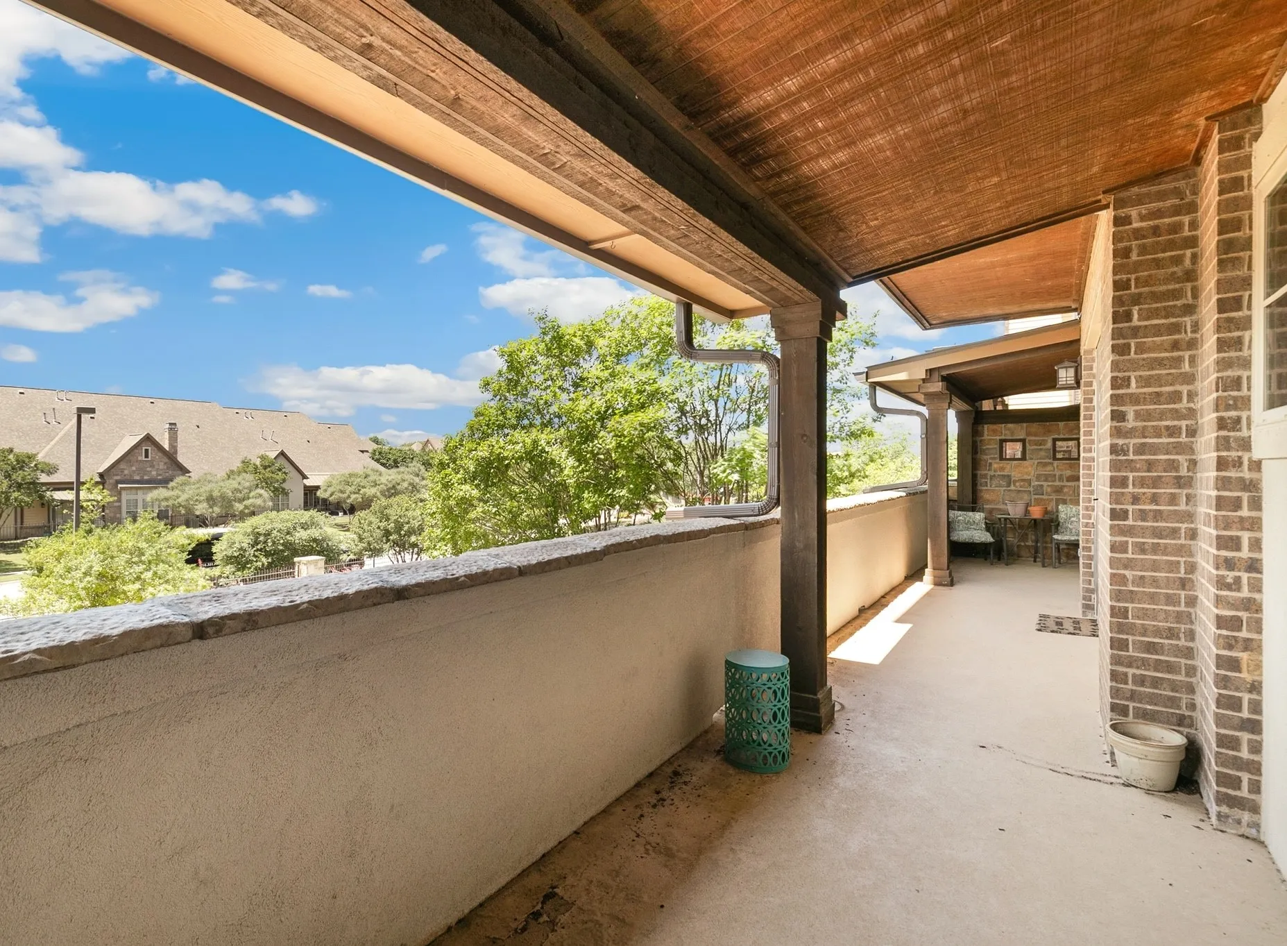 Expansive covered balcony featuring concrete flooring, a stucco and stone-capped half-wall, and a brick exterior wall