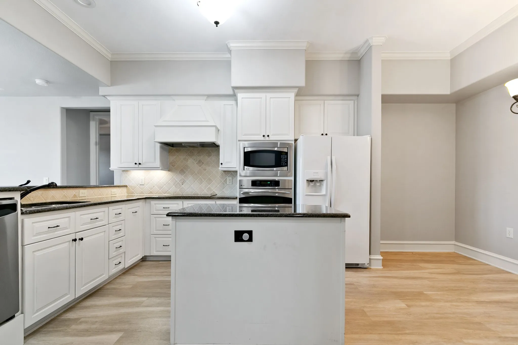White cabinetry with dark countertops, a tiled backsplash, and stainless steel appliances, including an integrated microwave and wall oven