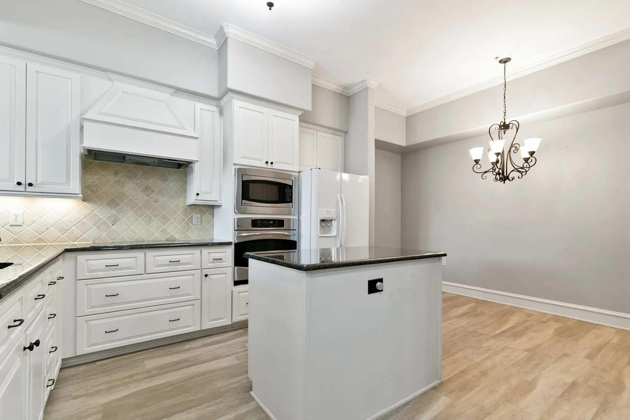 White cabinetry, stainless steel appliances, dark countertops, a decorative chandelier