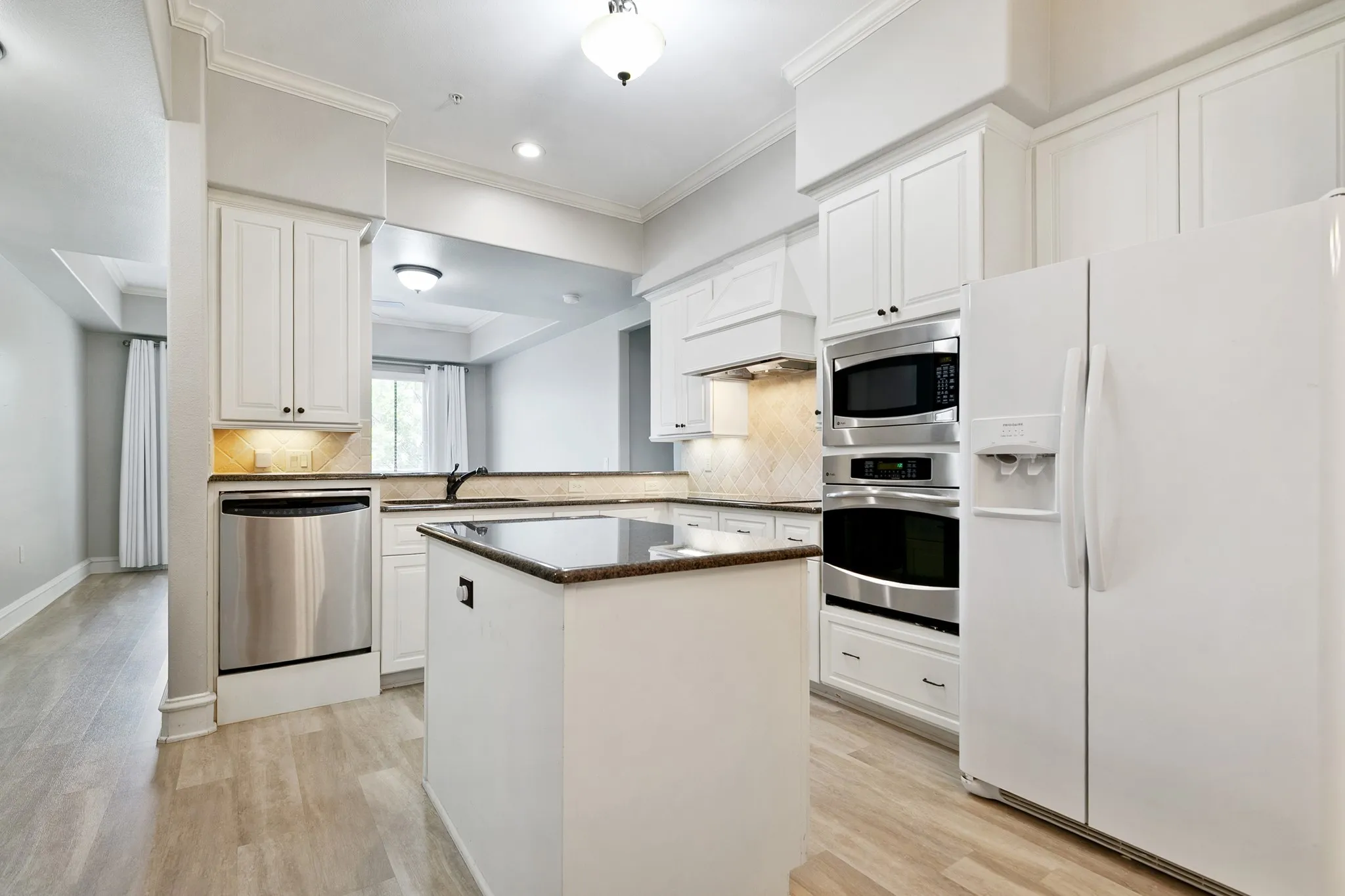 Kitchen with white cabinetry, stainless steel dishwasher, built-in double ovens, and a central island and a cooktop