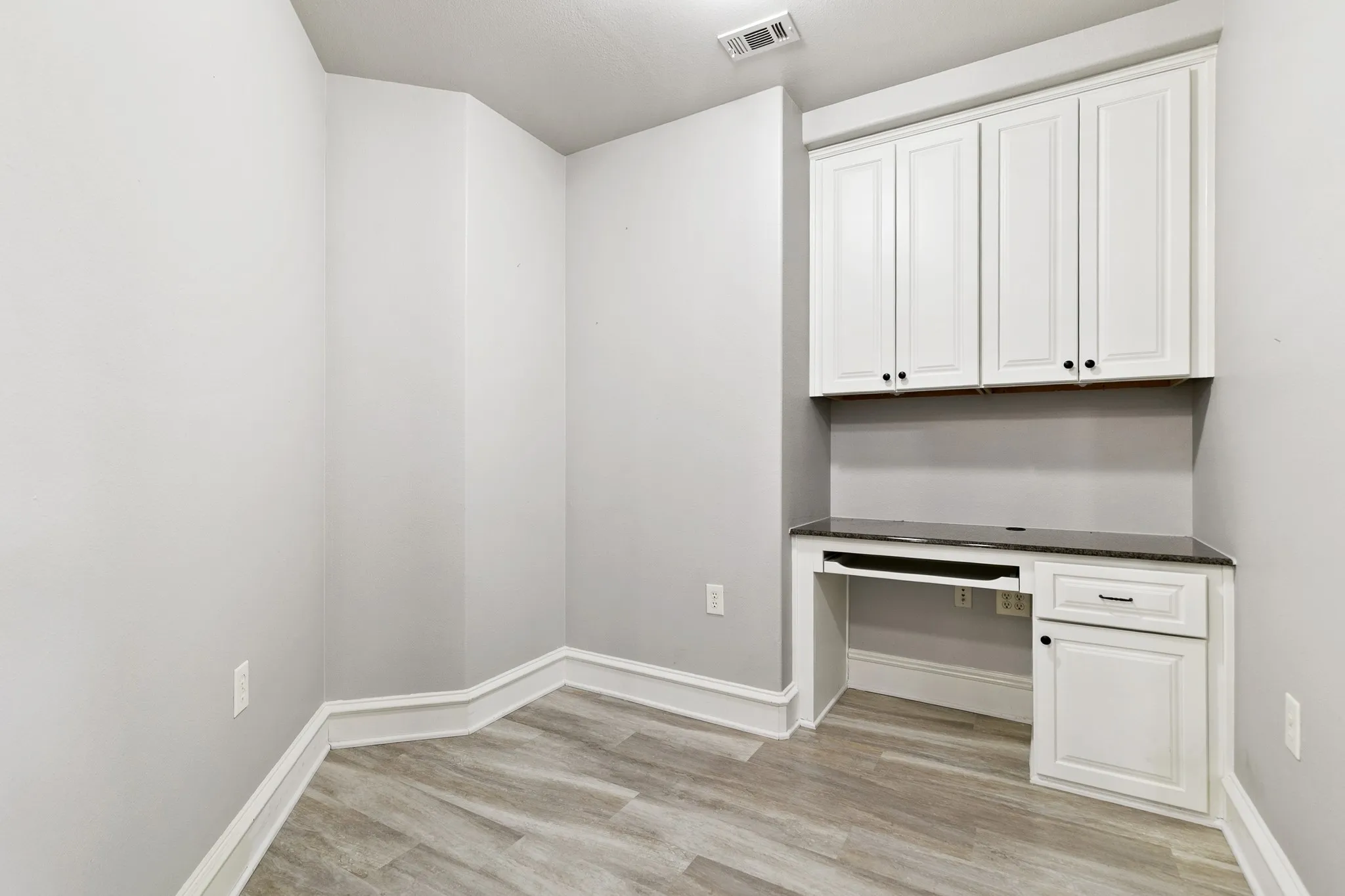 Built-in desk with a dark countertop, white shaker-style cabinetry, matte black hardware