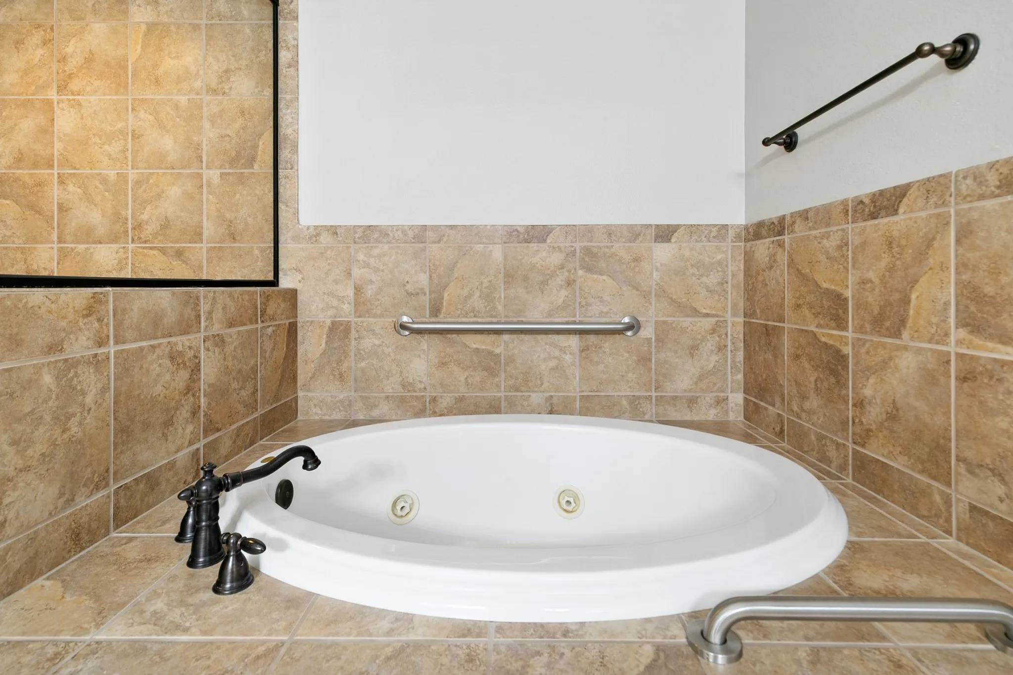 Jetted soaking tub with a bronze-finish faucet, surrounded by large format floor and wall tiles