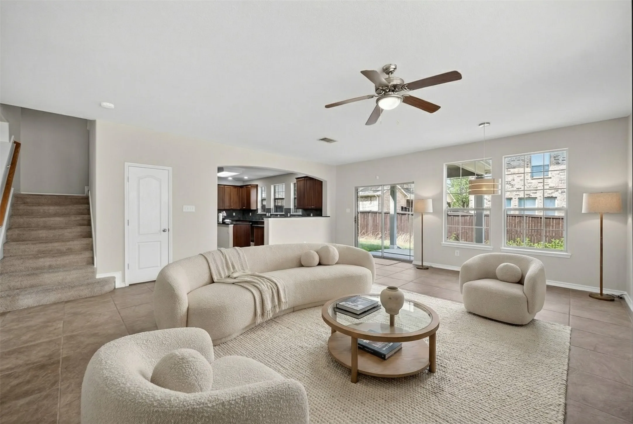 Tile flooring, overhead ceiling fan, multiple windows, sliding glass door, and staircase with wood handrail