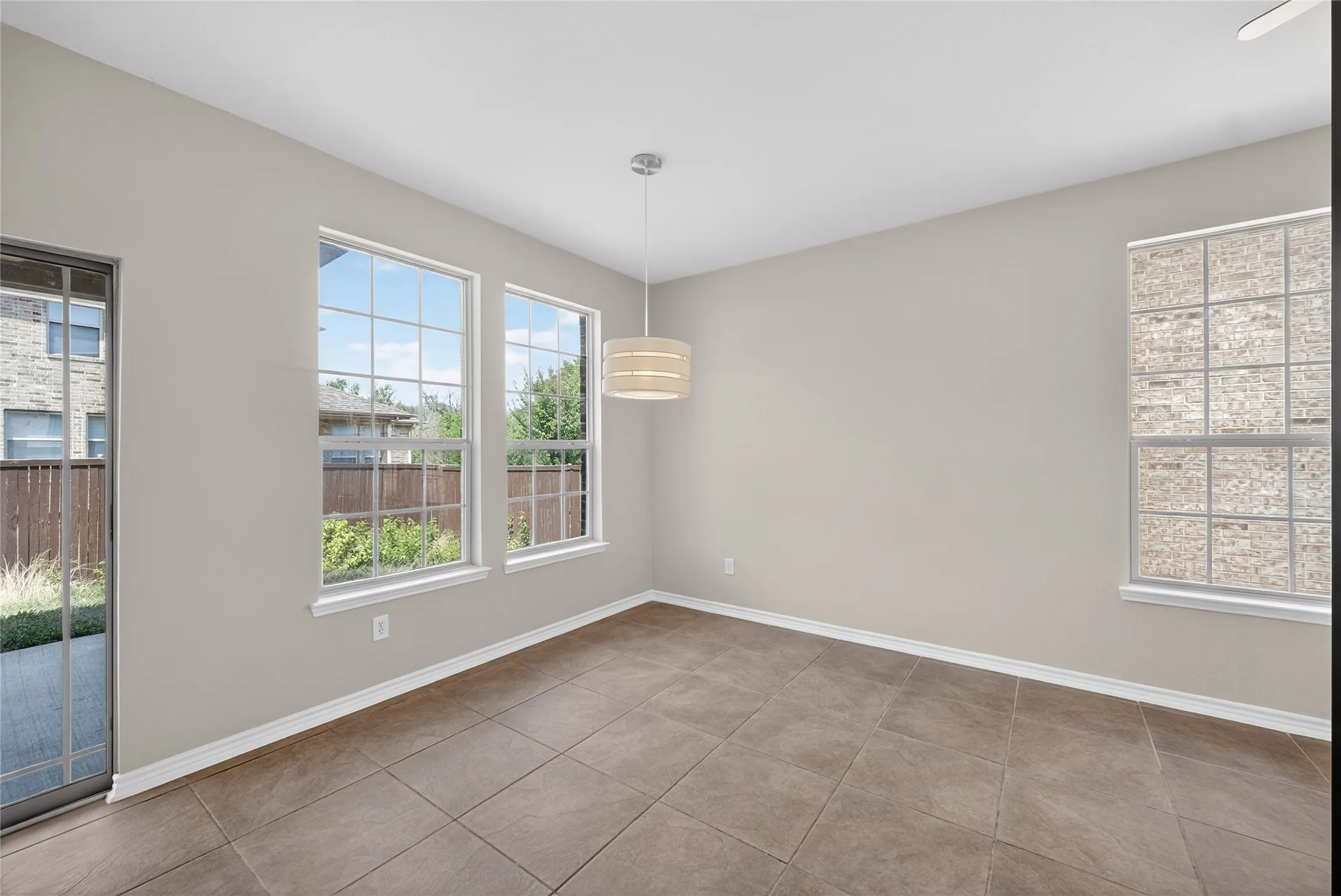 Tile flooring, multiple windows, a sliding glass door, and a drum pendant light fixture