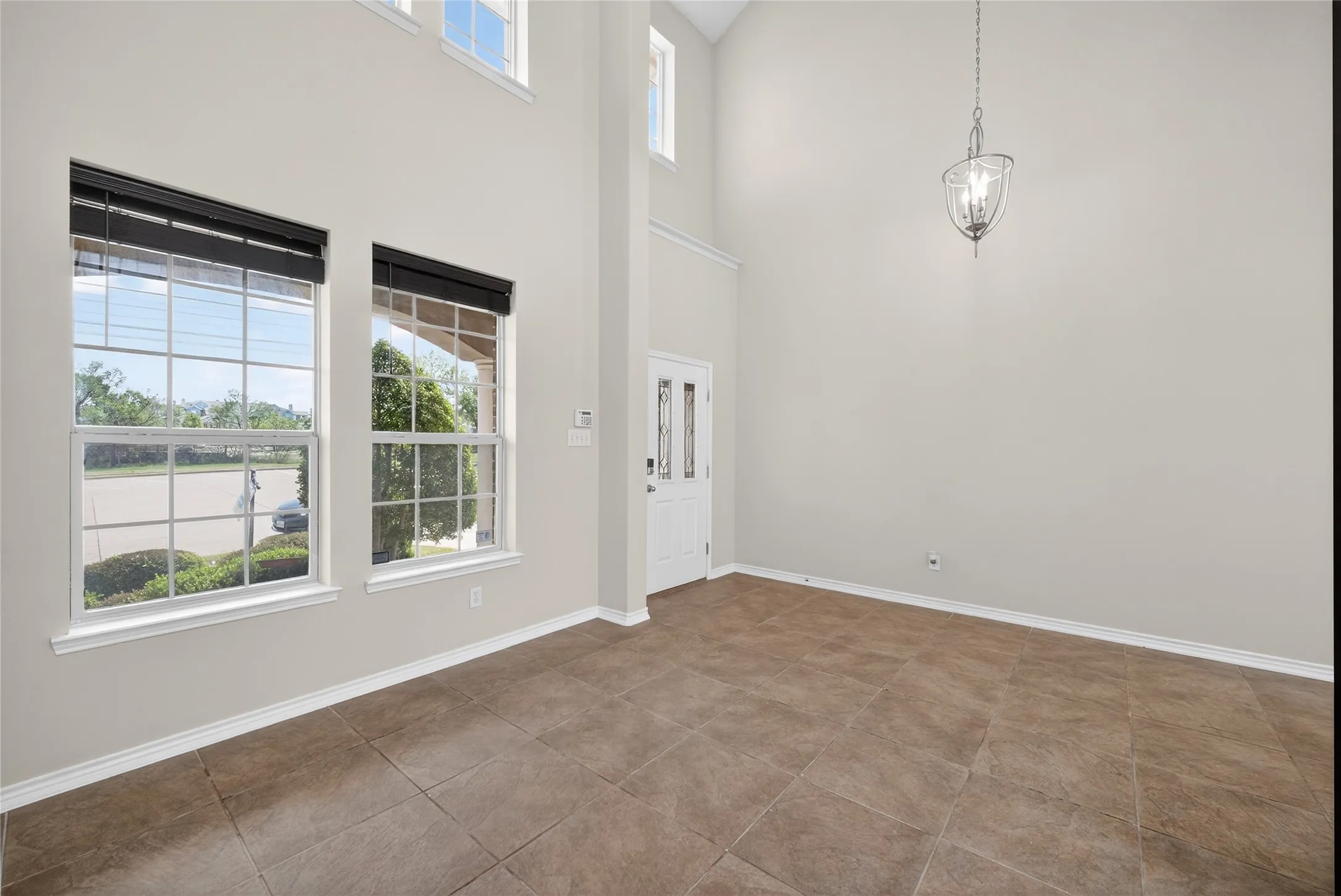 Two-story foyer with high ceilings, large grid windows, a glass-paneled front door, and a suspended chandelier