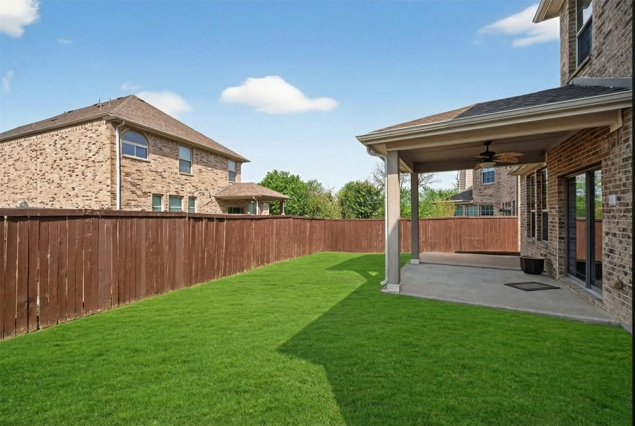 Expansive lawn with a wood-stained privacy fence, covered patio, and ceiling fan