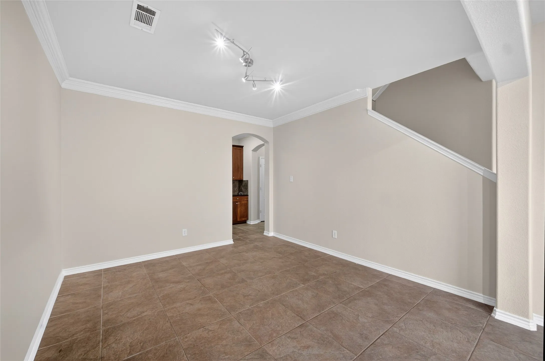 Neutral tone wall color, crown molding, tile flooring, track lighting, arched doorway
