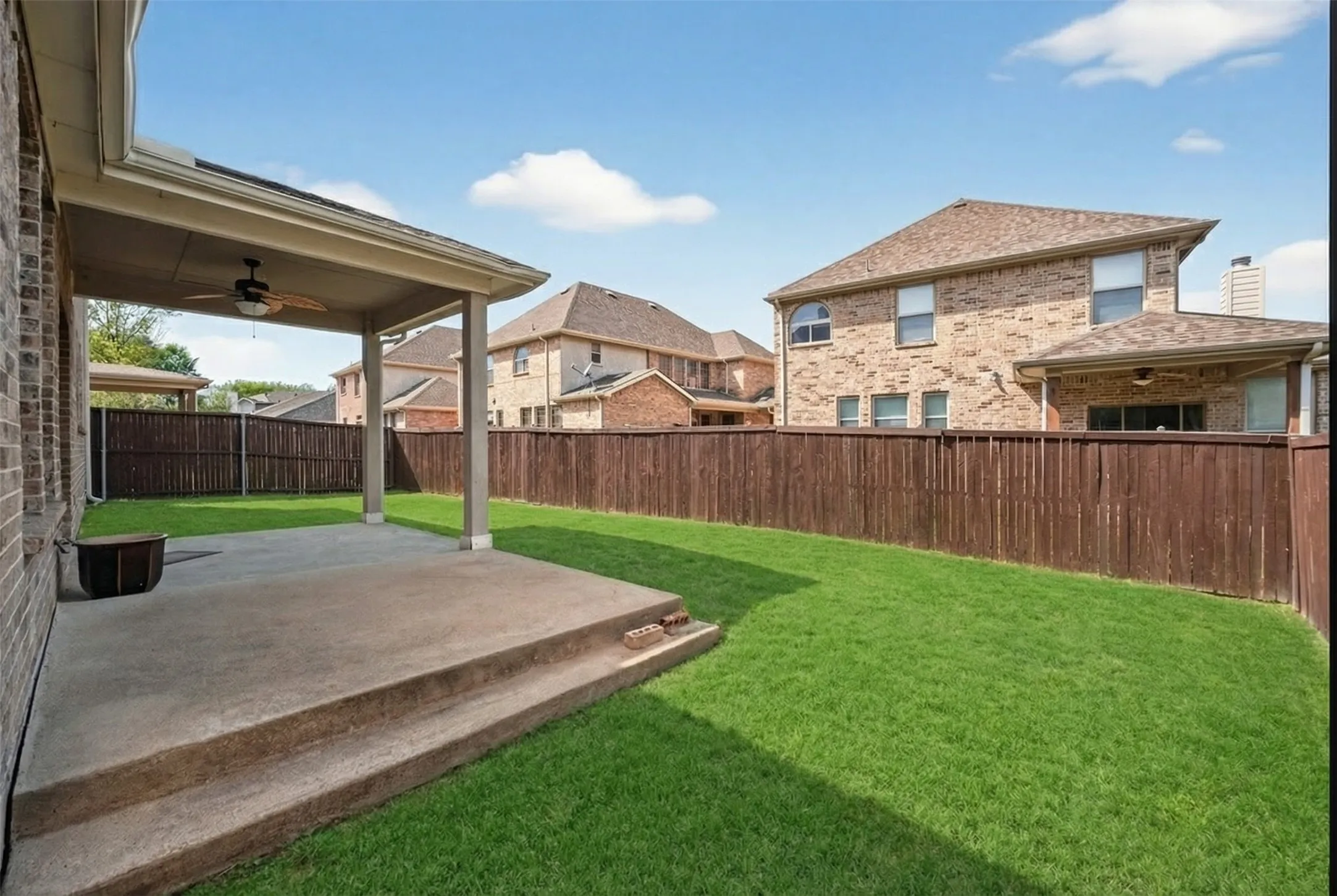 Expansive grassy yard with a covered patio featuring a built-in ceiling fan, and a wood privacy fence