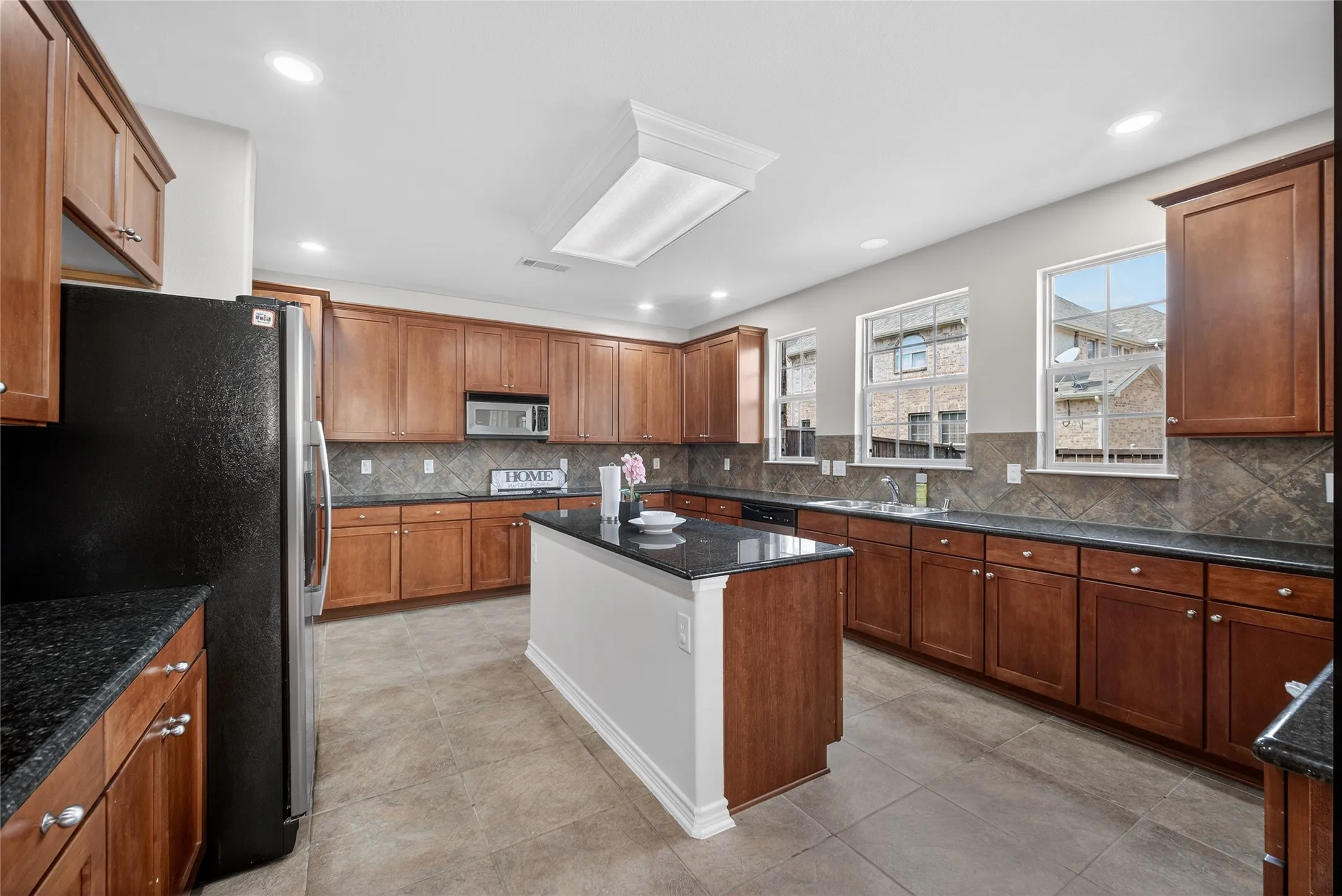 Kitchen featuring an island with a dark countertop, extensive wood cabinetry, tile flooring, and a tiled backsplash