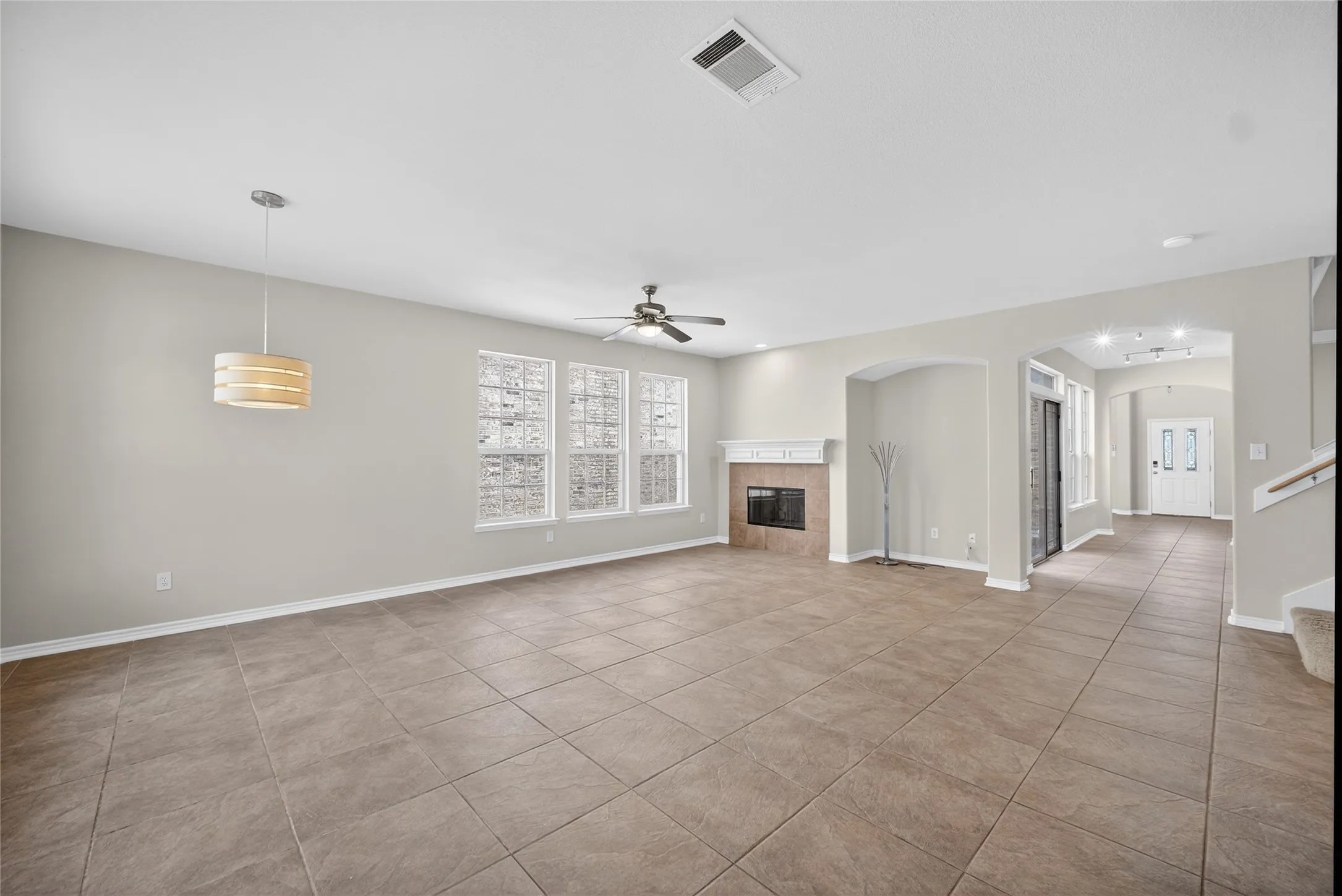 Tile flooring throughout, white mantel fireplace, multiple windows, ceiling fan, and pendant lighting