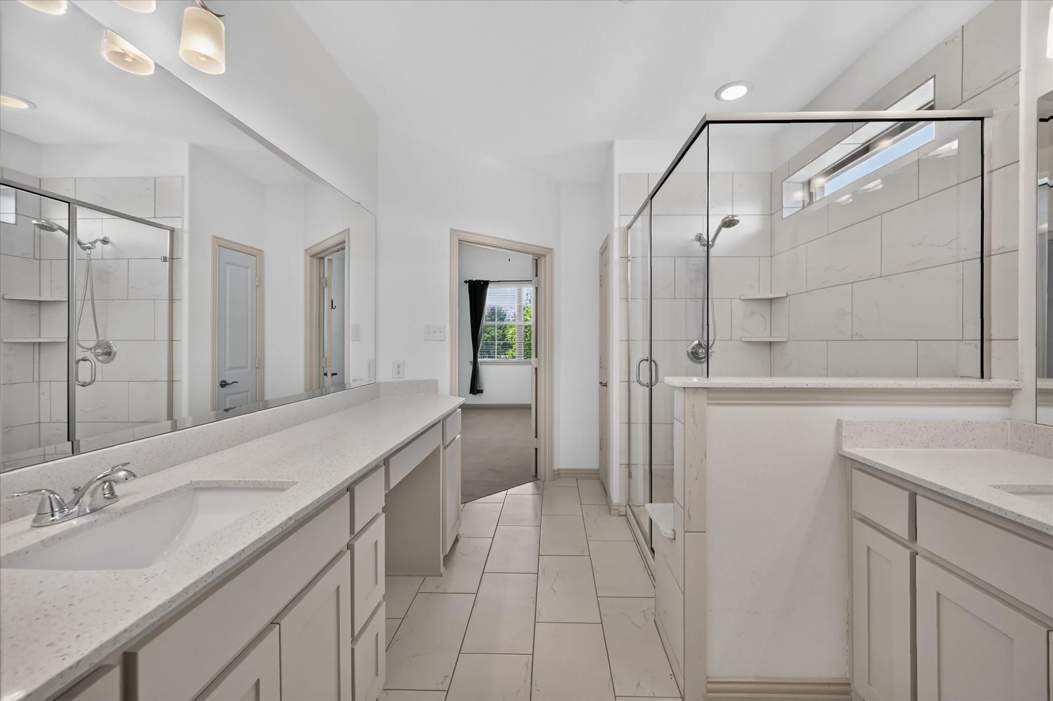 Dual vanity with integrated sinks, expansive wall-mounted mirror, glass-enclosed shower with tile surround, separate vanity area, and tiled flooring