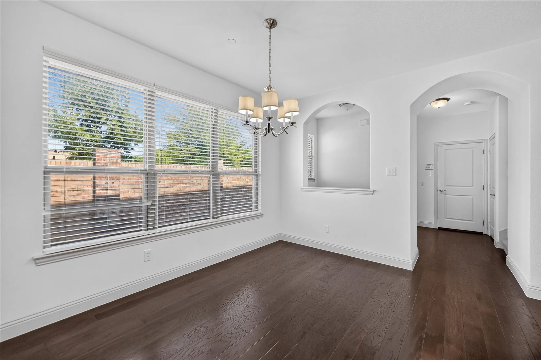 Dark wood-finish flooring, a multi-pane window with blinds, an arched doorway, and a built-in wall niche with an arch