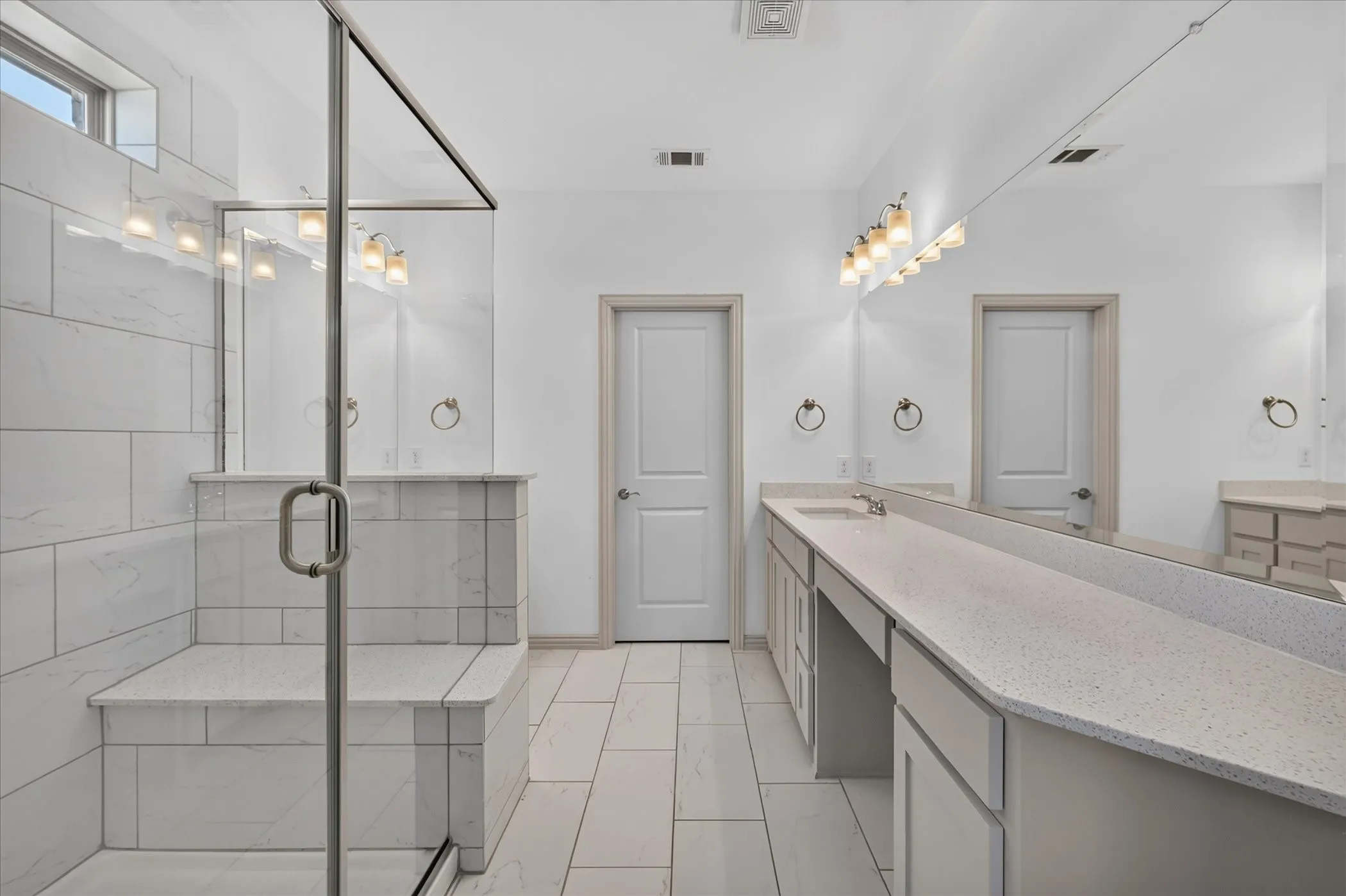 Frameless glass shower enclosure with a built-in bench, complemented by white tiled walls and flooring