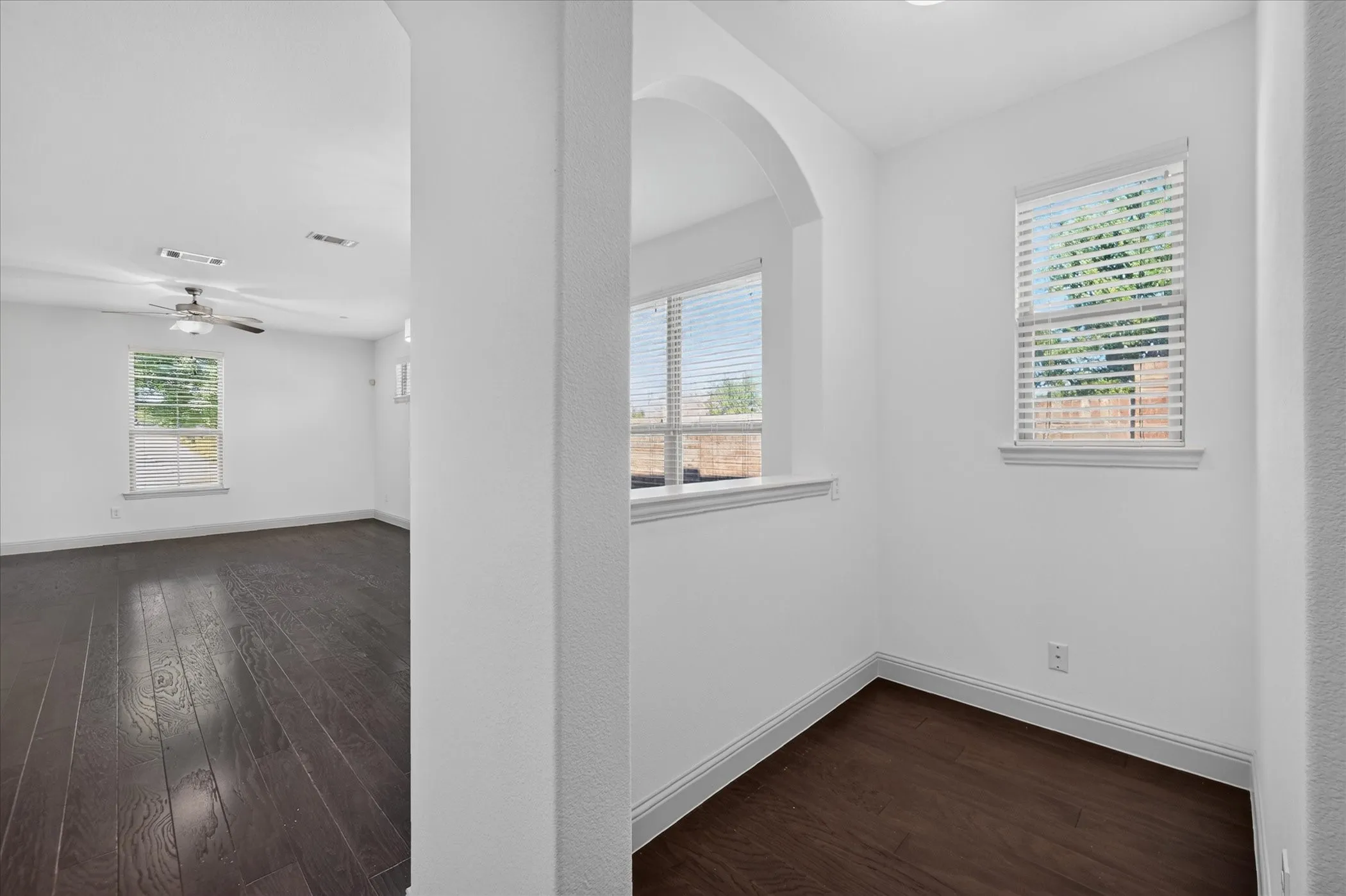 Dark wood-finish flooring throughout, white painted walls, arched architectural detail, and two windows with blinds