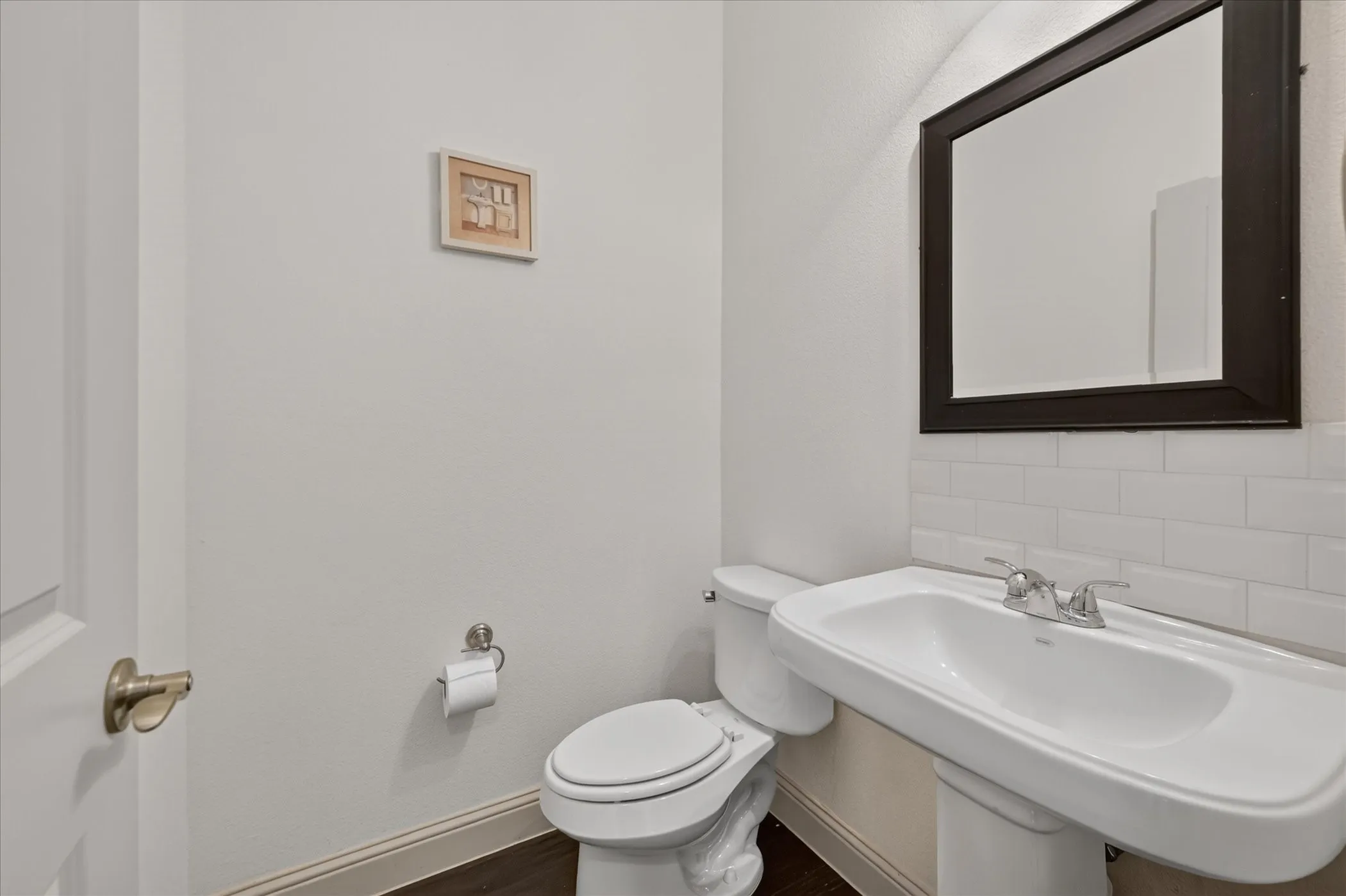 Pedestal sink with chrome faucet, subway tile backsplash, and a framed wall mirror