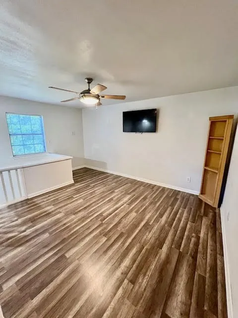Wood-finish flooring, ceiling fan with integrated lighting, and a window with white trim